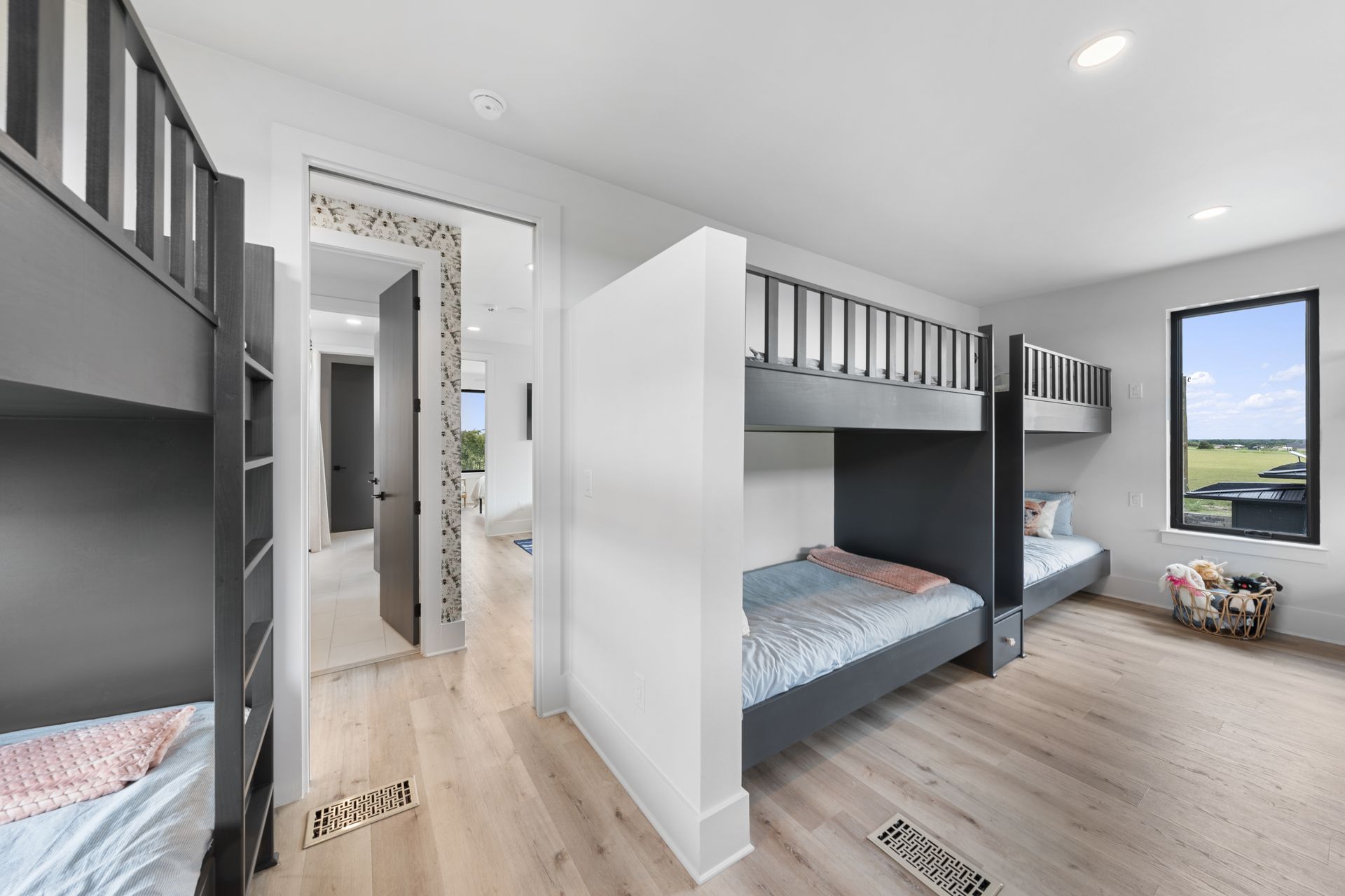 Modern bedroom with gray bunk beds, white walls, wood floor, and a large window showing greenery