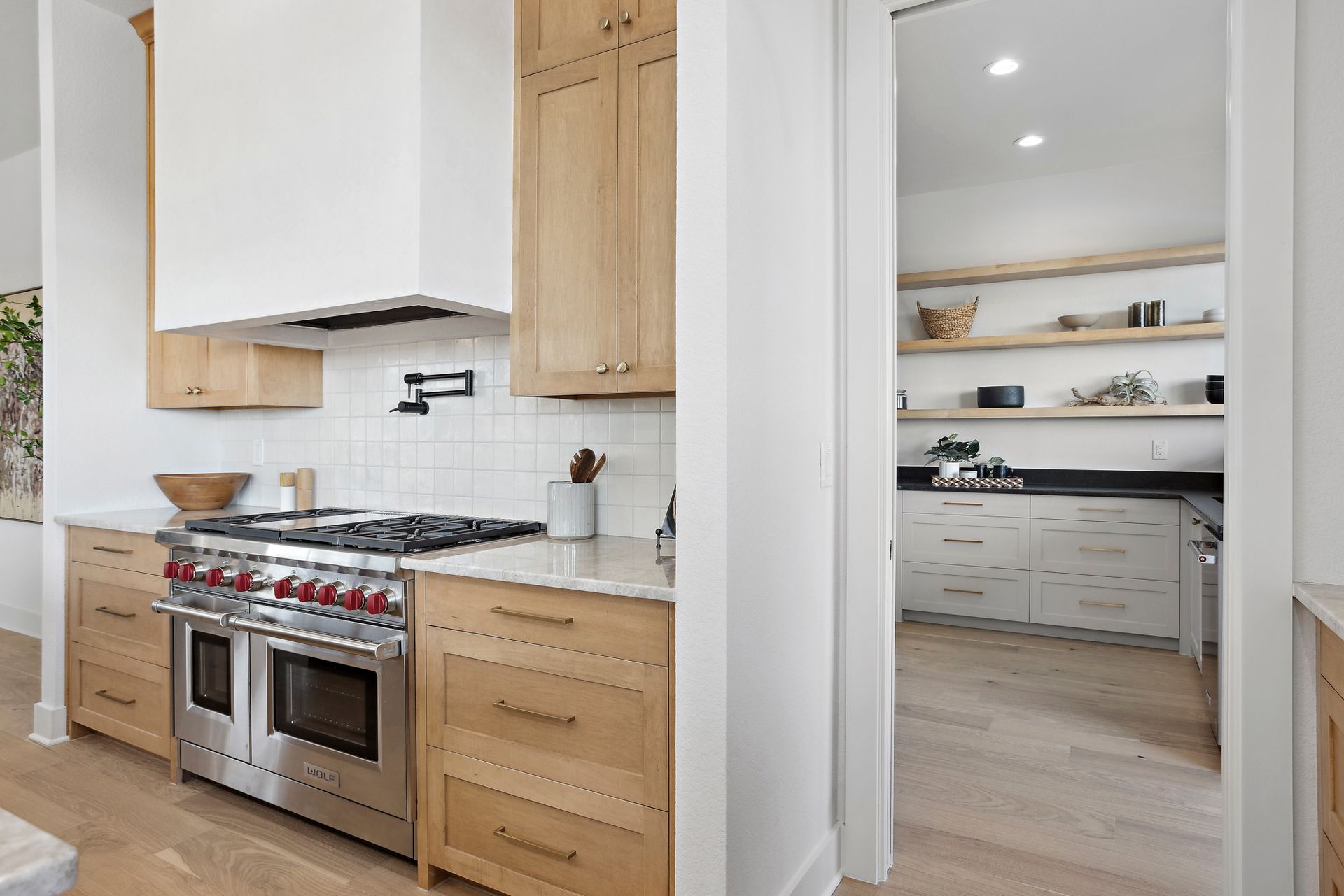 Modern kitchen with stainless steel stove, white cabinets, and open pantry doorway