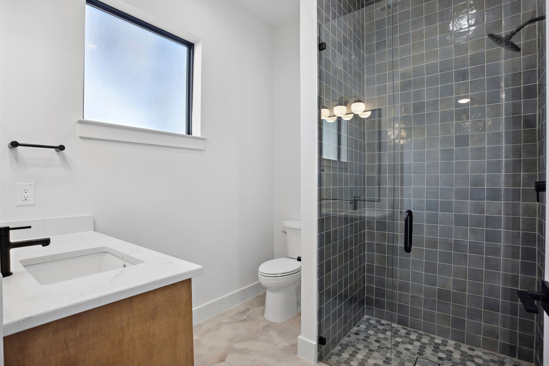 Modern bathroom with white vanity, toilet, window, and glass-enclosed tiled shower