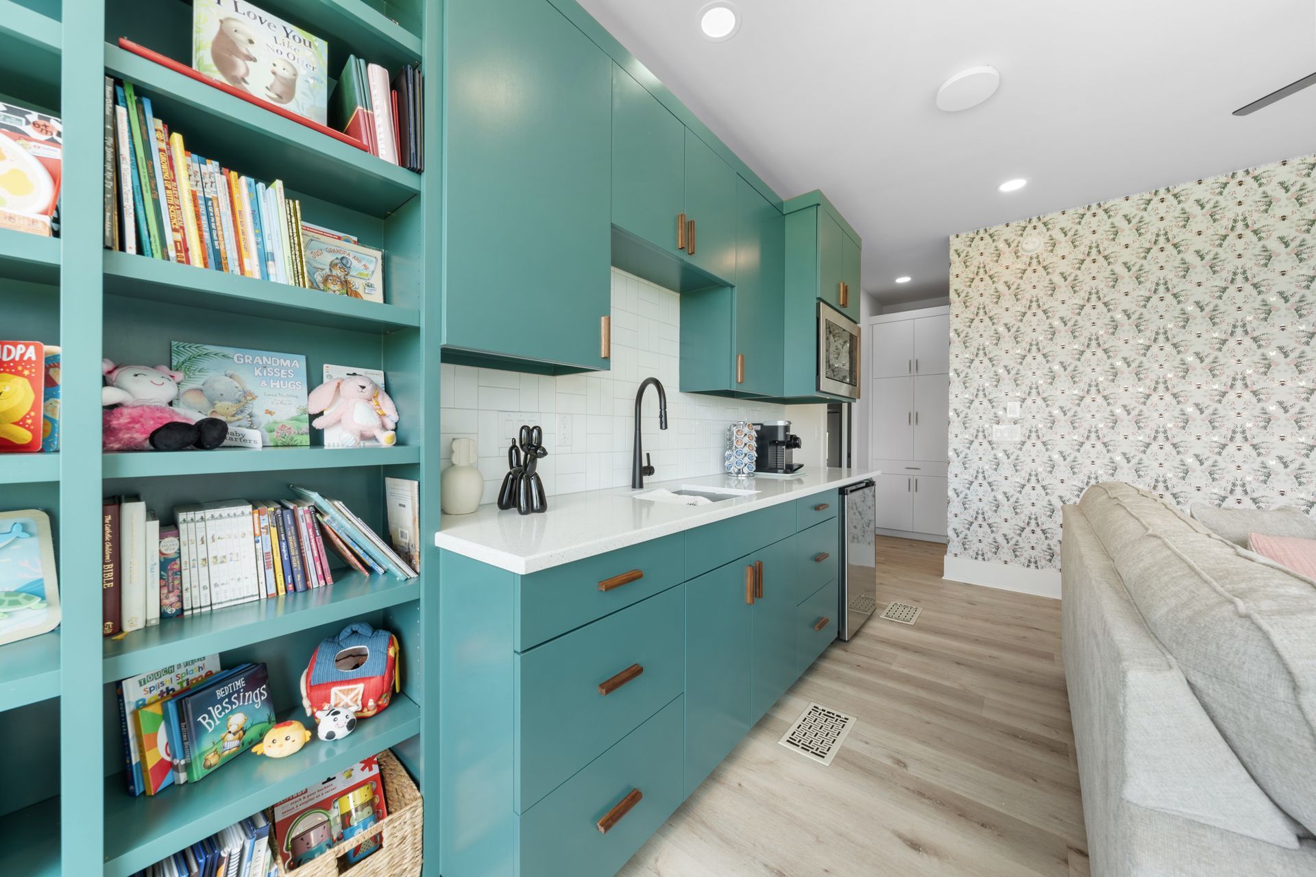 Teal built-in shelves and cabinets in a bright modern room with books, toys, and a gray sofa