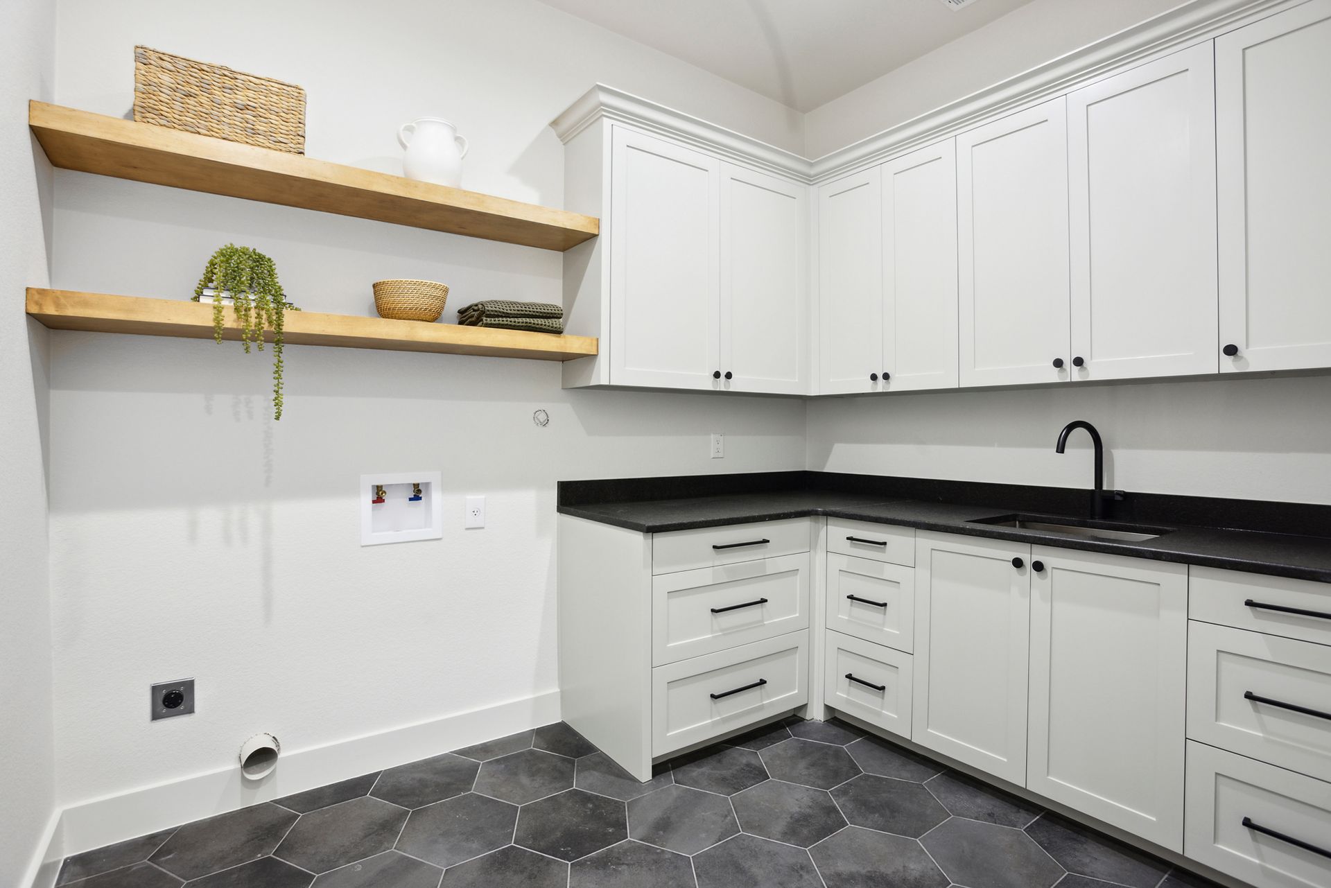 Modern white kitchen with black countertops, open wooden shelves, and gray patterned tile floor