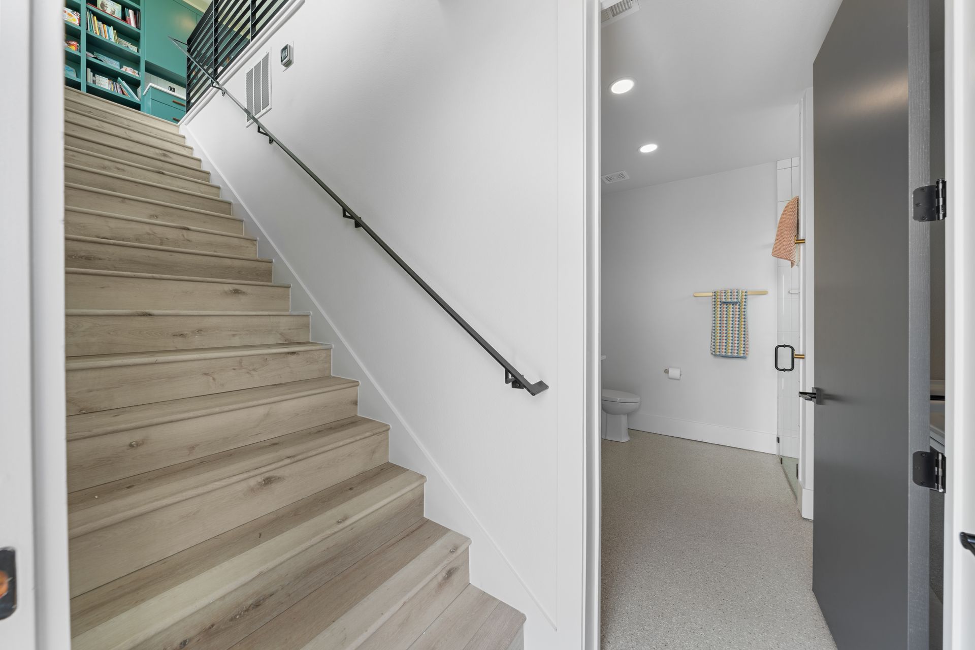 Modern stairwell with white walls, wooden steps, and a doorway to a bright room with carpet
