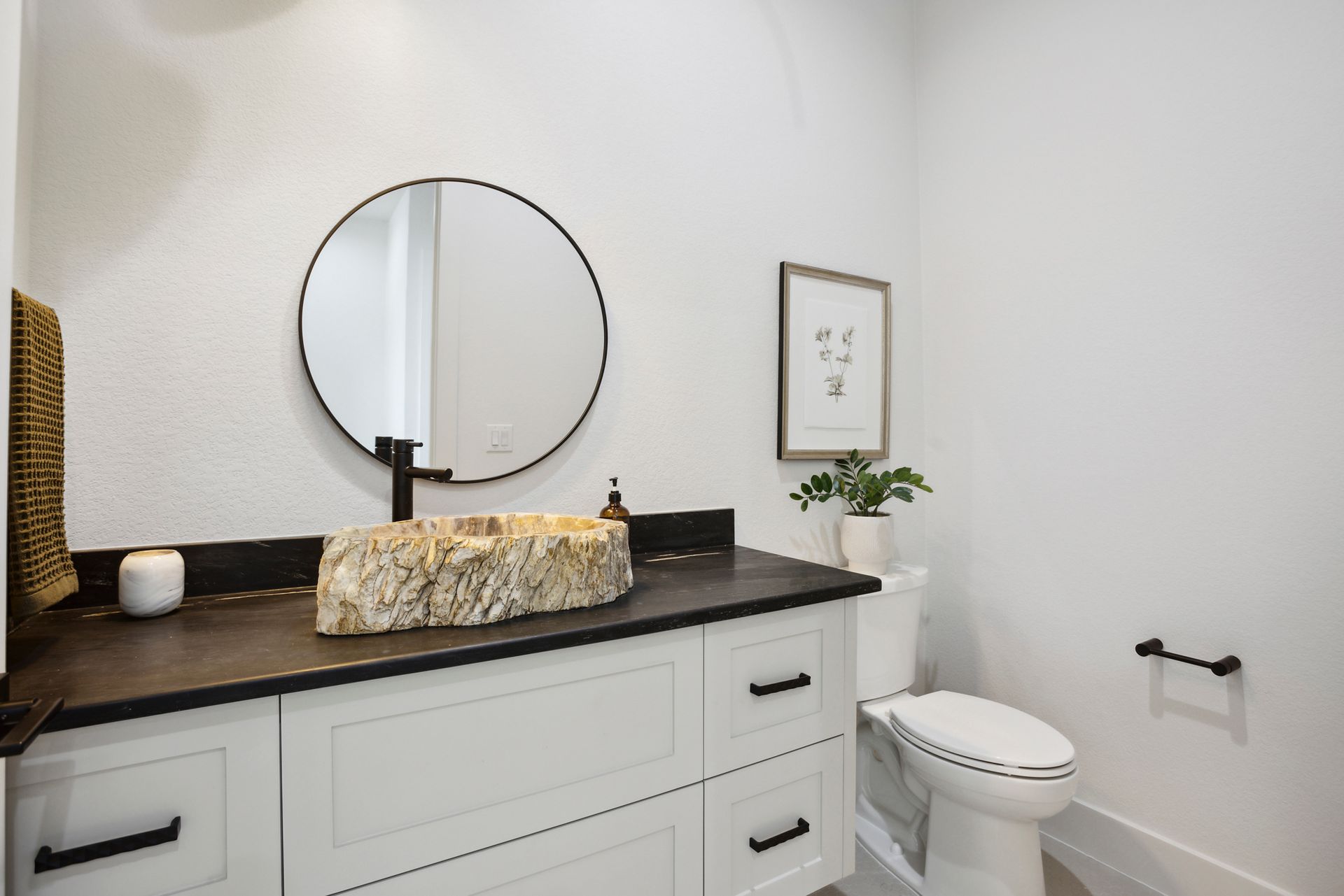 Modern bathroom vanity with round mirror, countertop decor, and toilet beside it