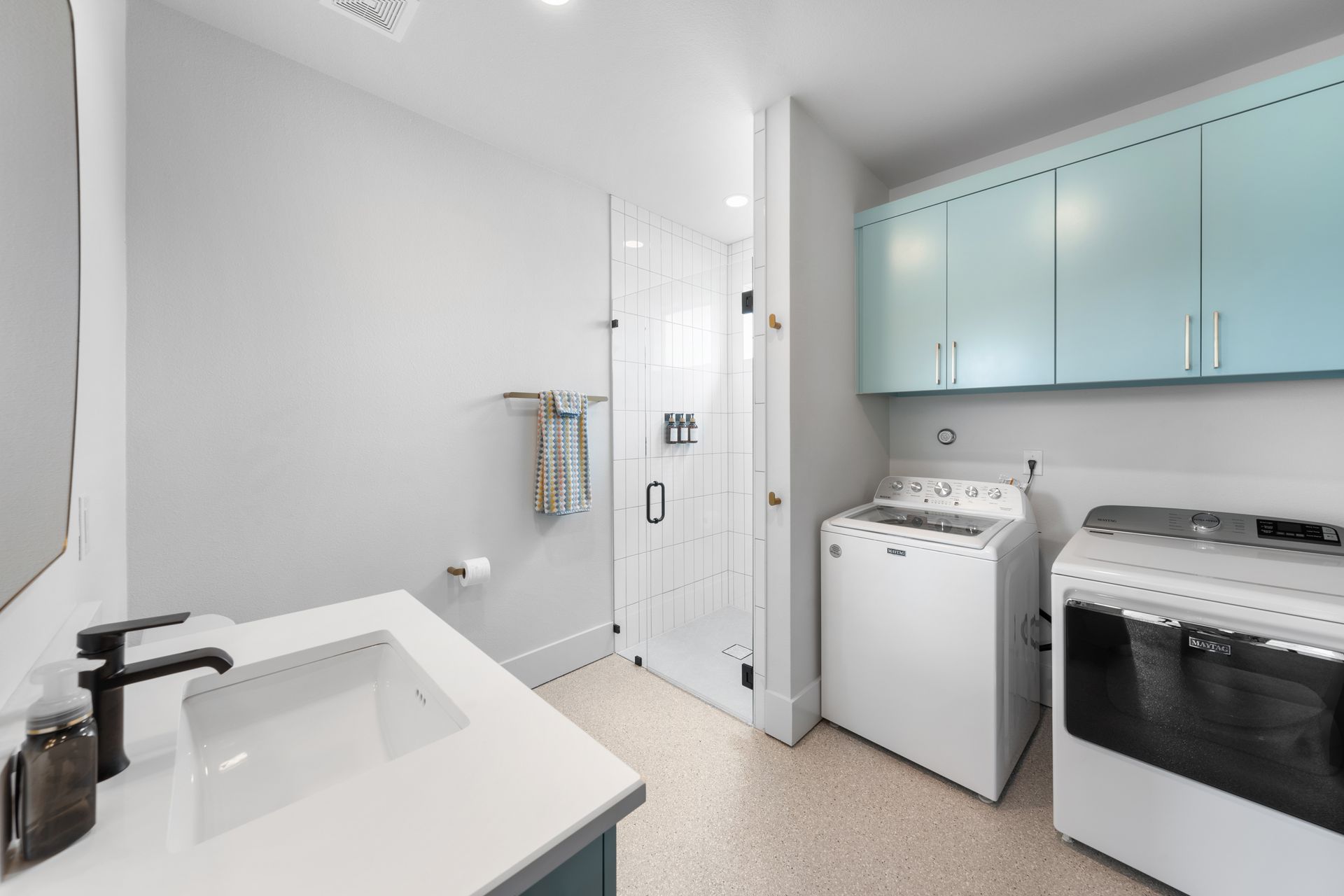 Bright laundry room with sink, washer, dryer, and light blue cabinets