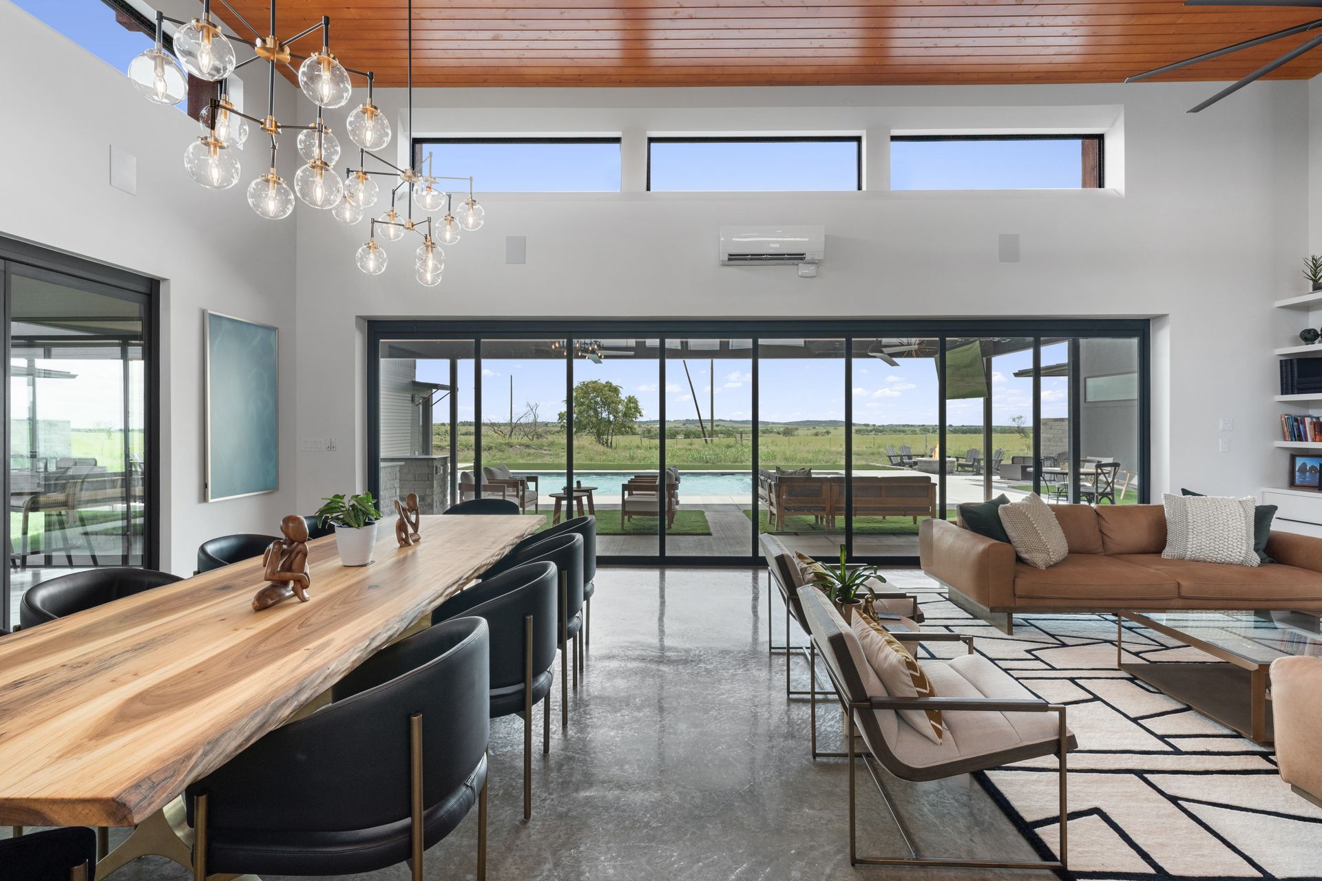 Modern open living room with wood ceiling, large glass doors, dining table, and sectional sofa overlooking a view