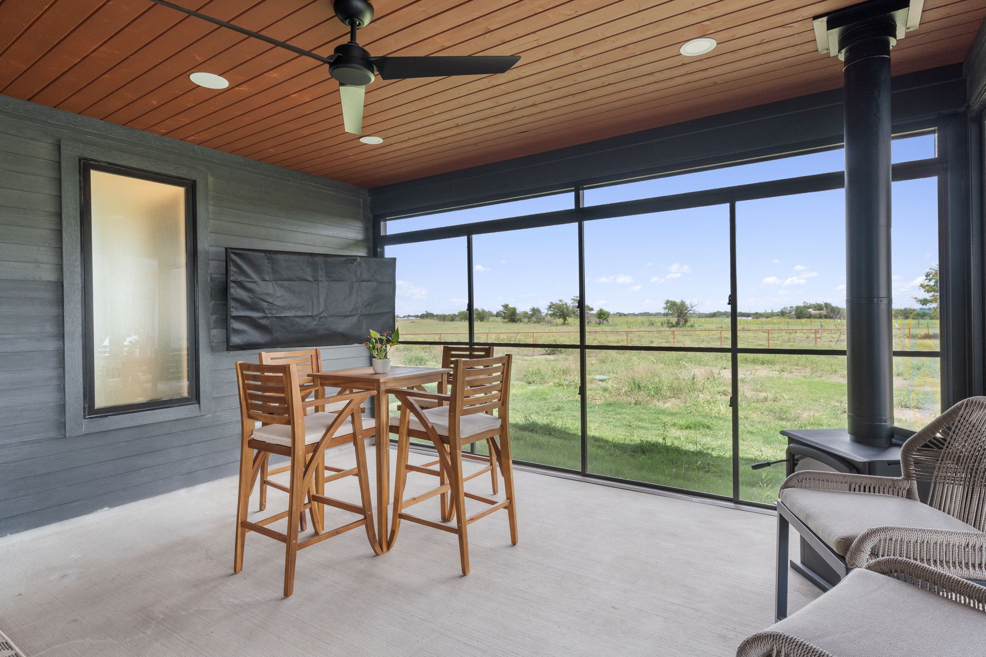 Covered patio with bar table and stools, ceiling fan, fireplace, and screened view of a grassy yard