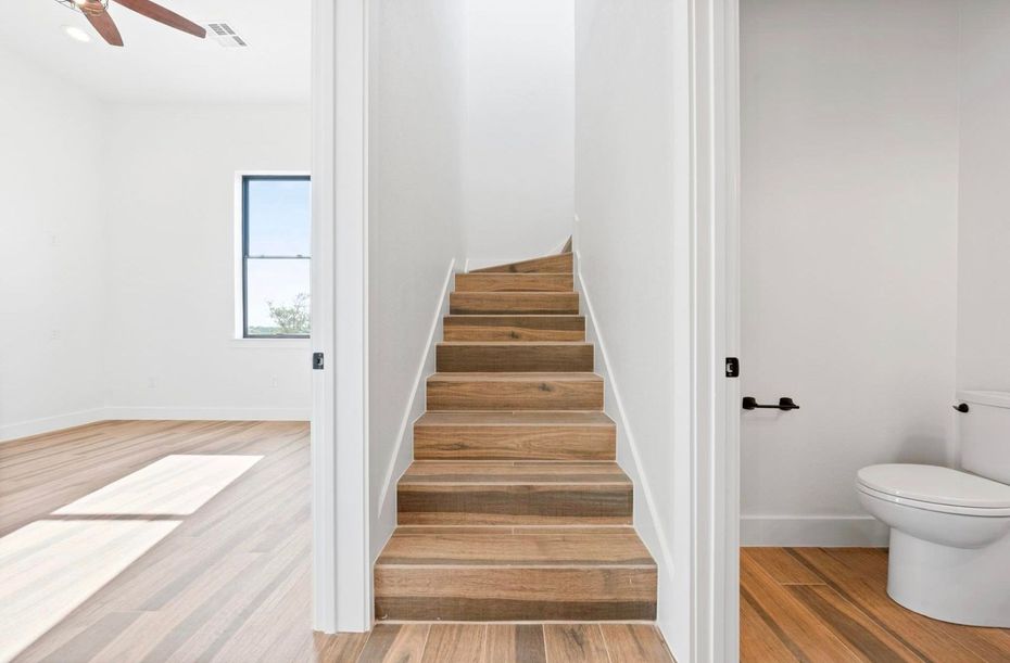Bright hallway with wooden stairs between a sunlit room and a bathroom with a toilet