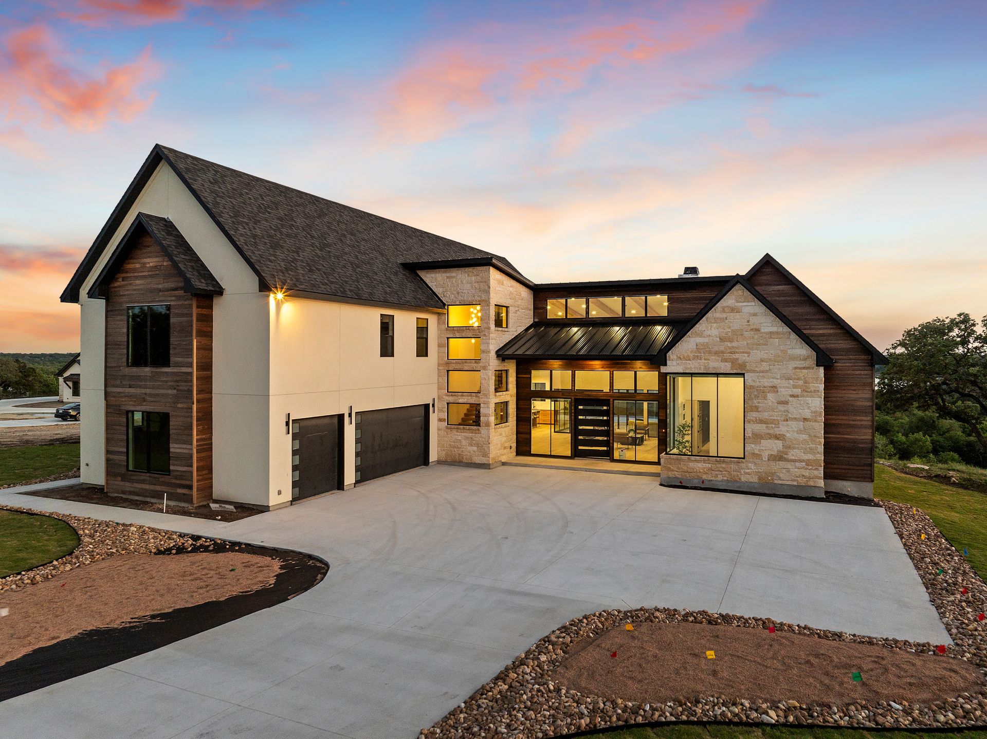 Modern two-story house with stone accents and a large driveway at sunset