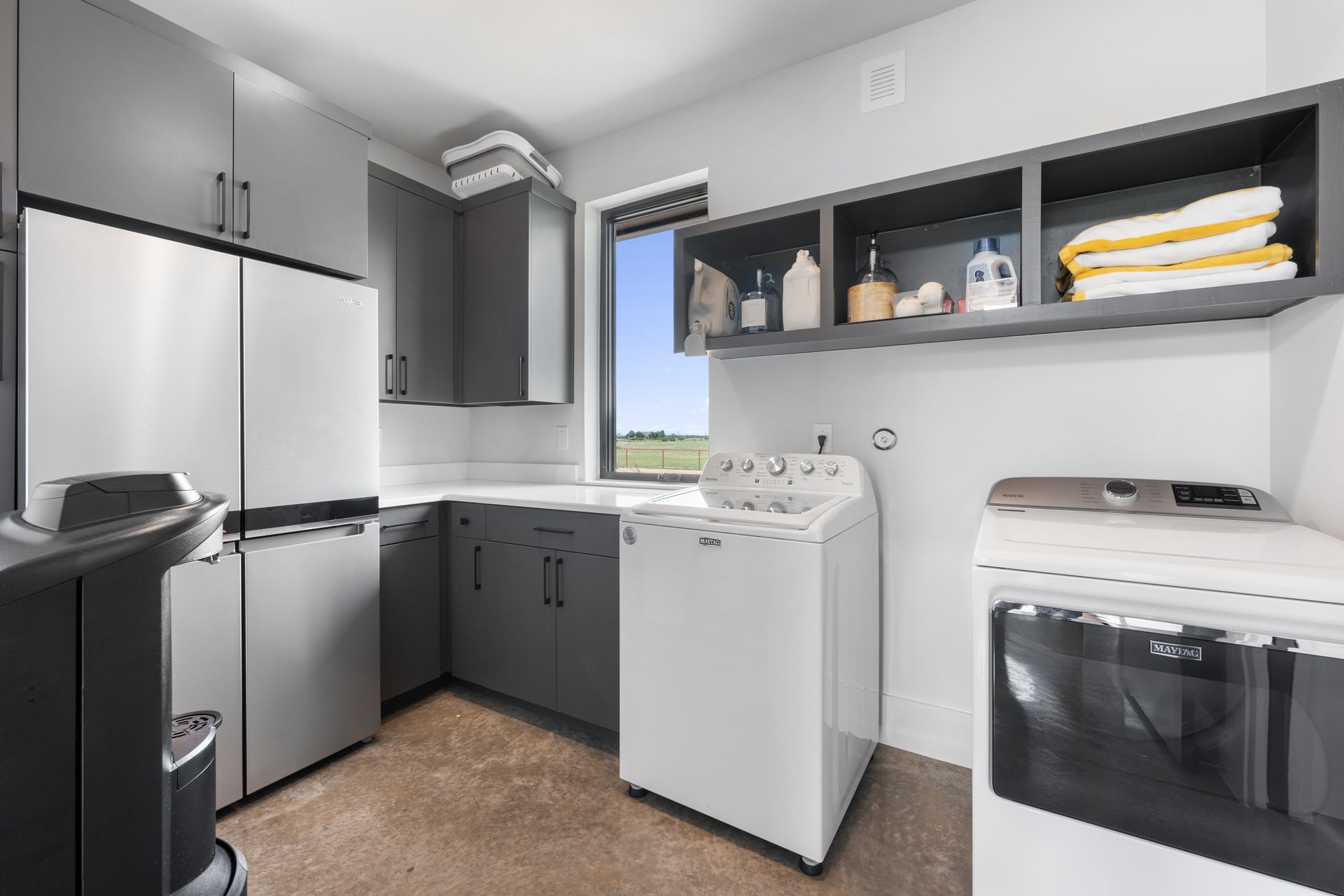 Small laundry room with gray cabinets, washer, dryer, refrigerator, and open shelves.