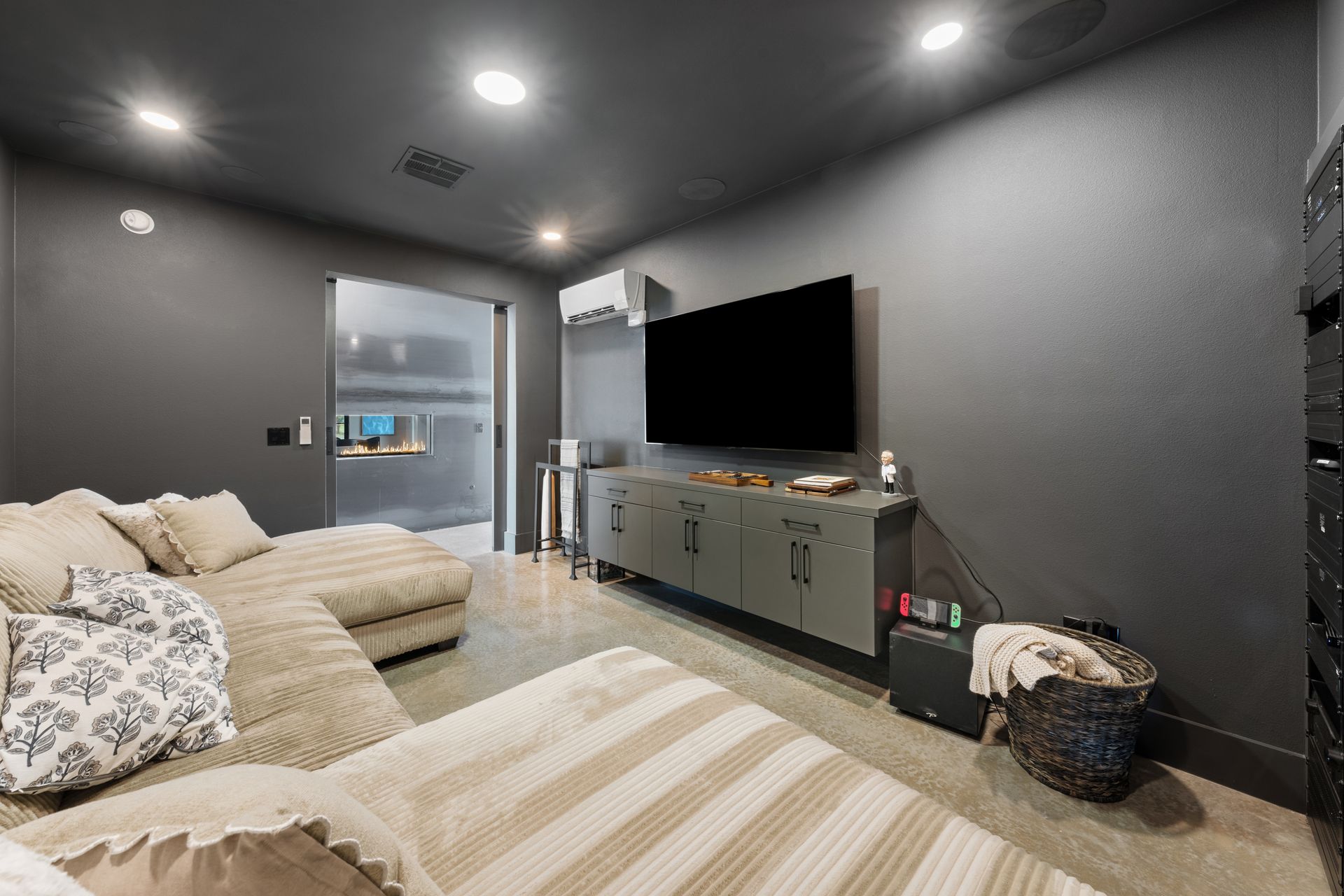 Modern living room with beige couches, a large TV, and gray walls under recessed ceiling lights