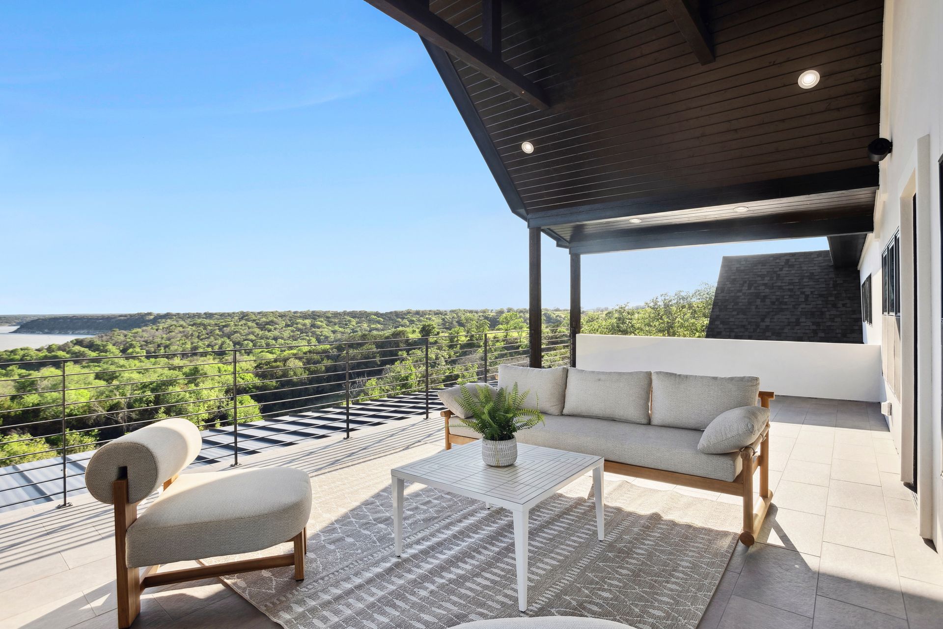 Modern balcony with cream outdoor seating, white table, and scenic treetop view under a shaded roof