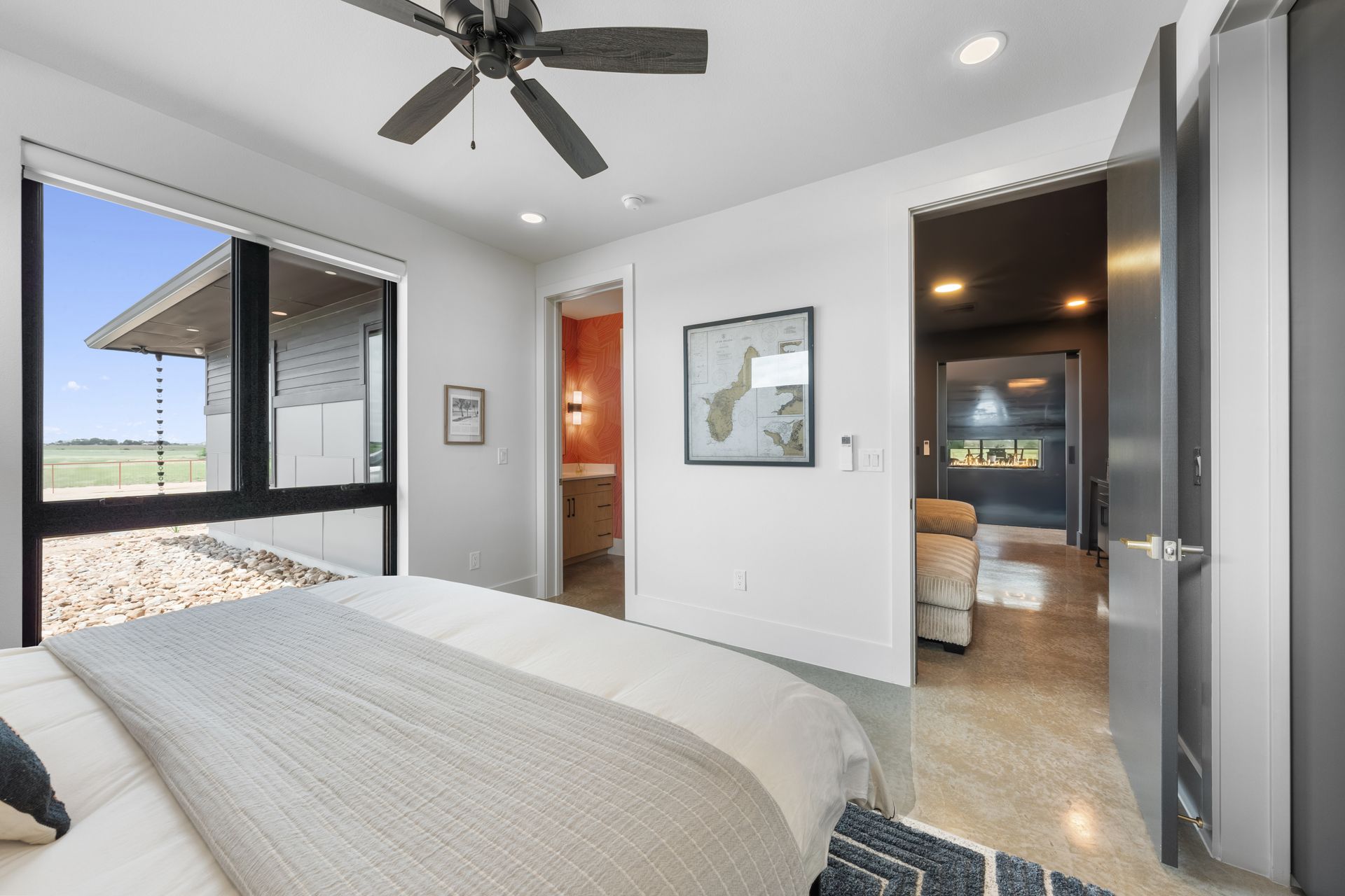 Bright bedroom with queen bed, ceiling fan, open patio door, and view into adjoining bathroom.