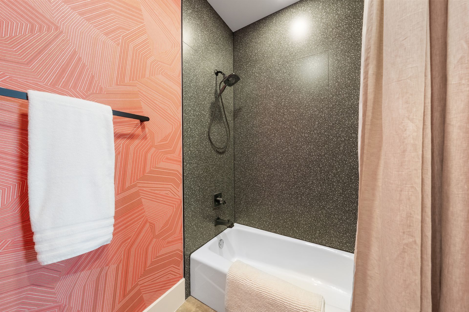 Modern bathroom with shower, white tub, coral textured wall, and towel rack with white towel