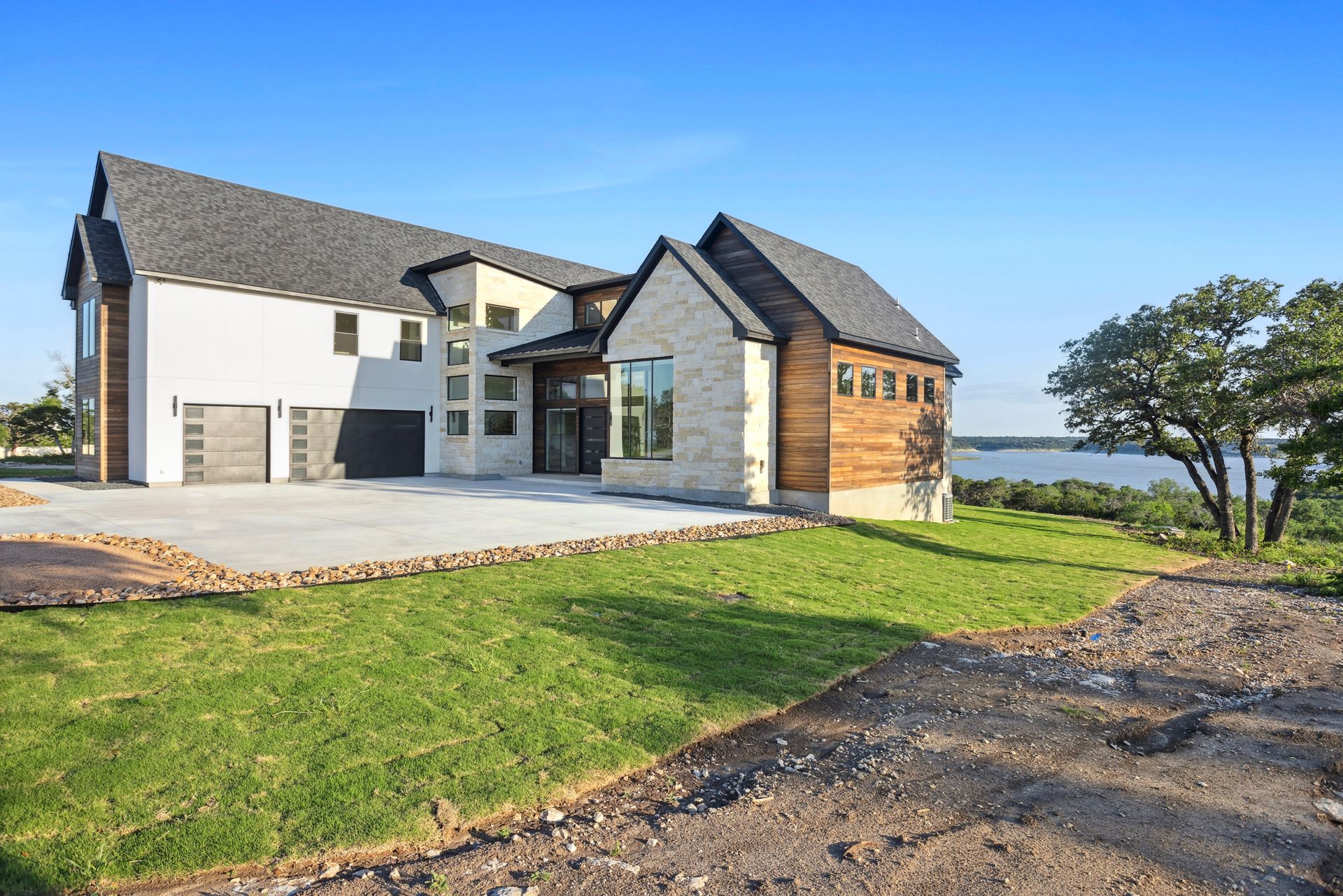 Modern house with stone and wood exterior beside a grassy lot under a clear blue sky
