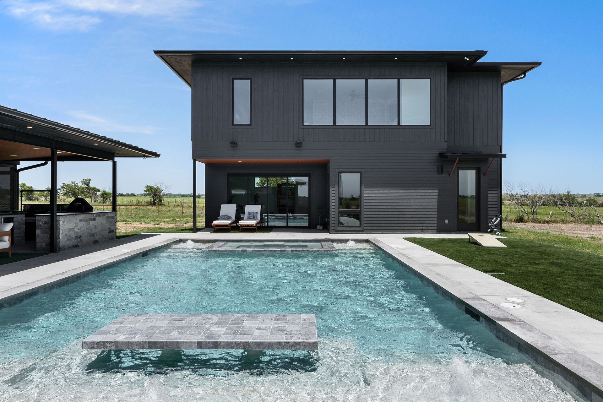 Modern two-story black house with a swimming pool and patio by open fields