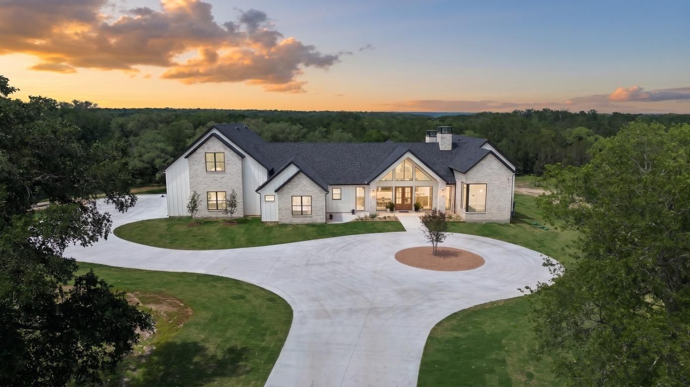 Modern single-story house at dusk with a large circular driveway and landscaped front yard