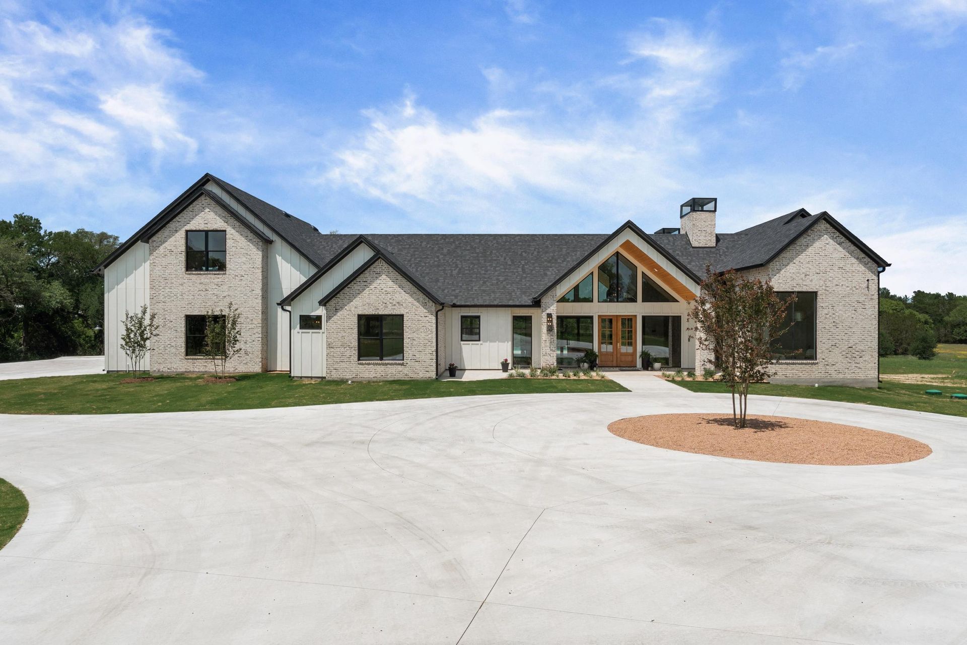 Large modern stone house with dark roof and wide driveway under a blue sky