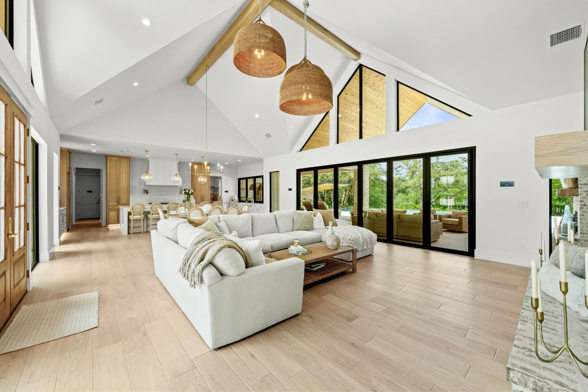Bright, airy open-plan living room with white sofa, wood floors, and large windows overlooking greenery