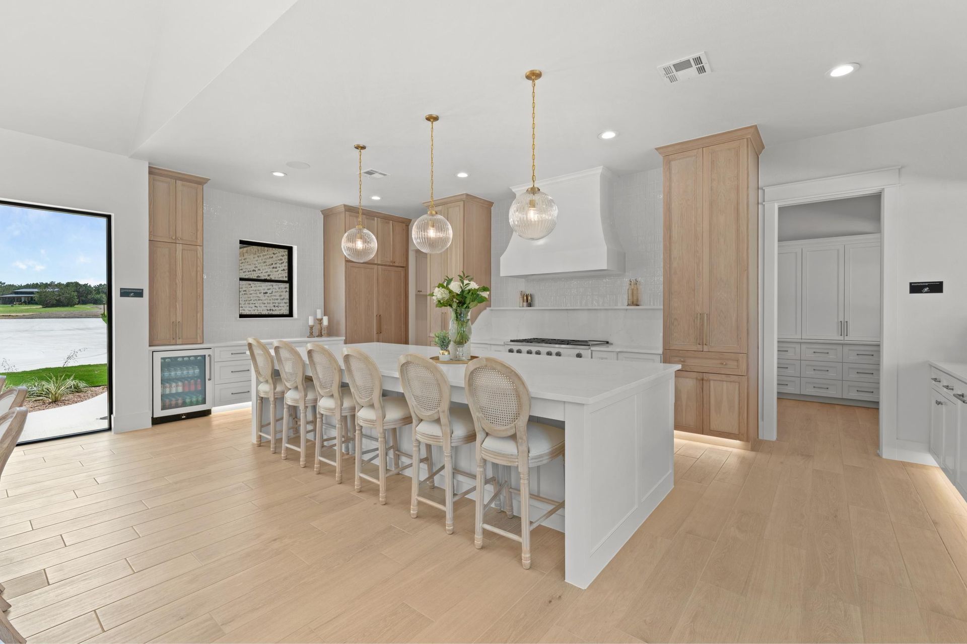 Bright modern kitchen with white island, six upholstered stools, gold pendant lights, and light wood floors