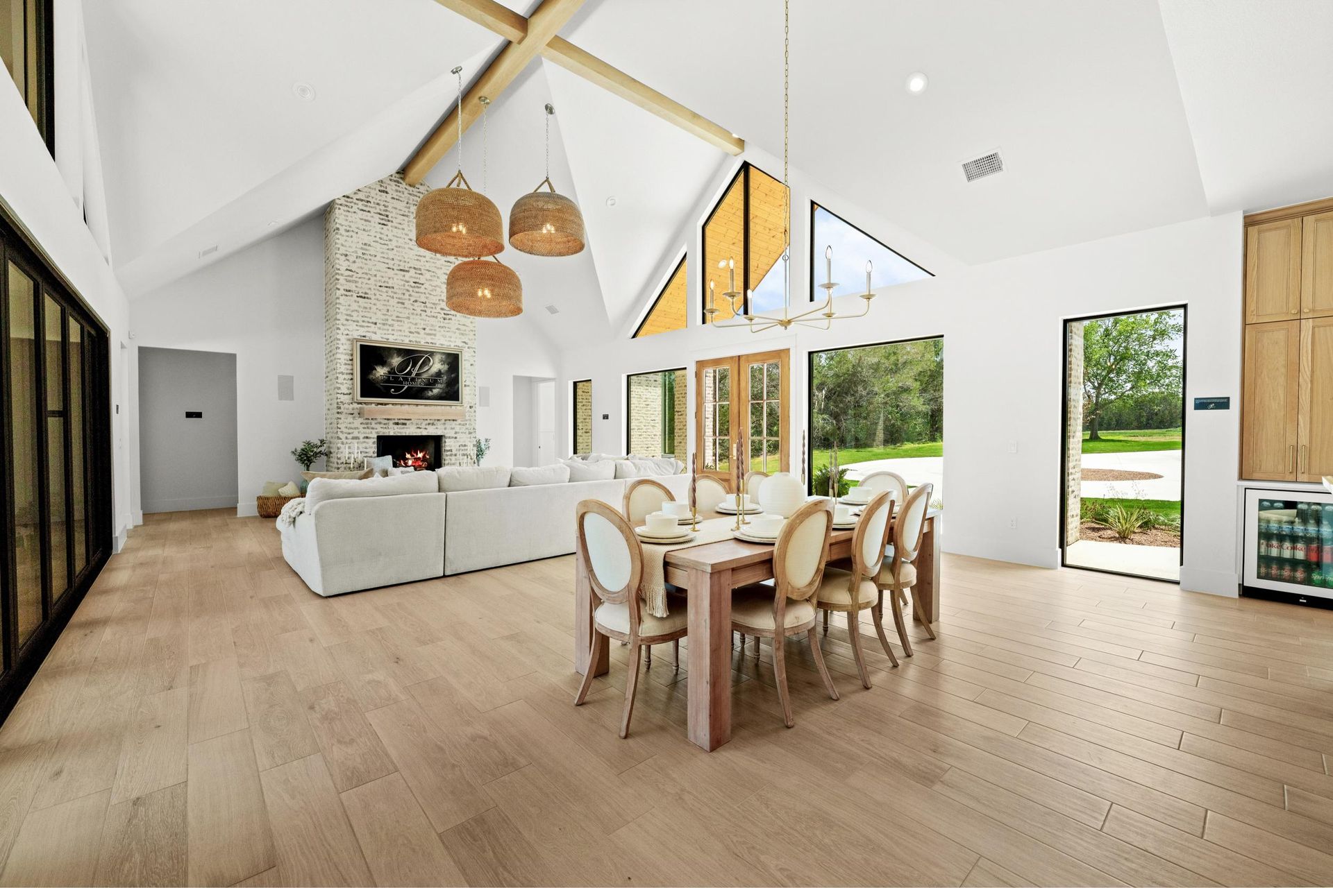 Bright open-plan living and dining room with high ceilings, wood floors, white furniture, and large windows.