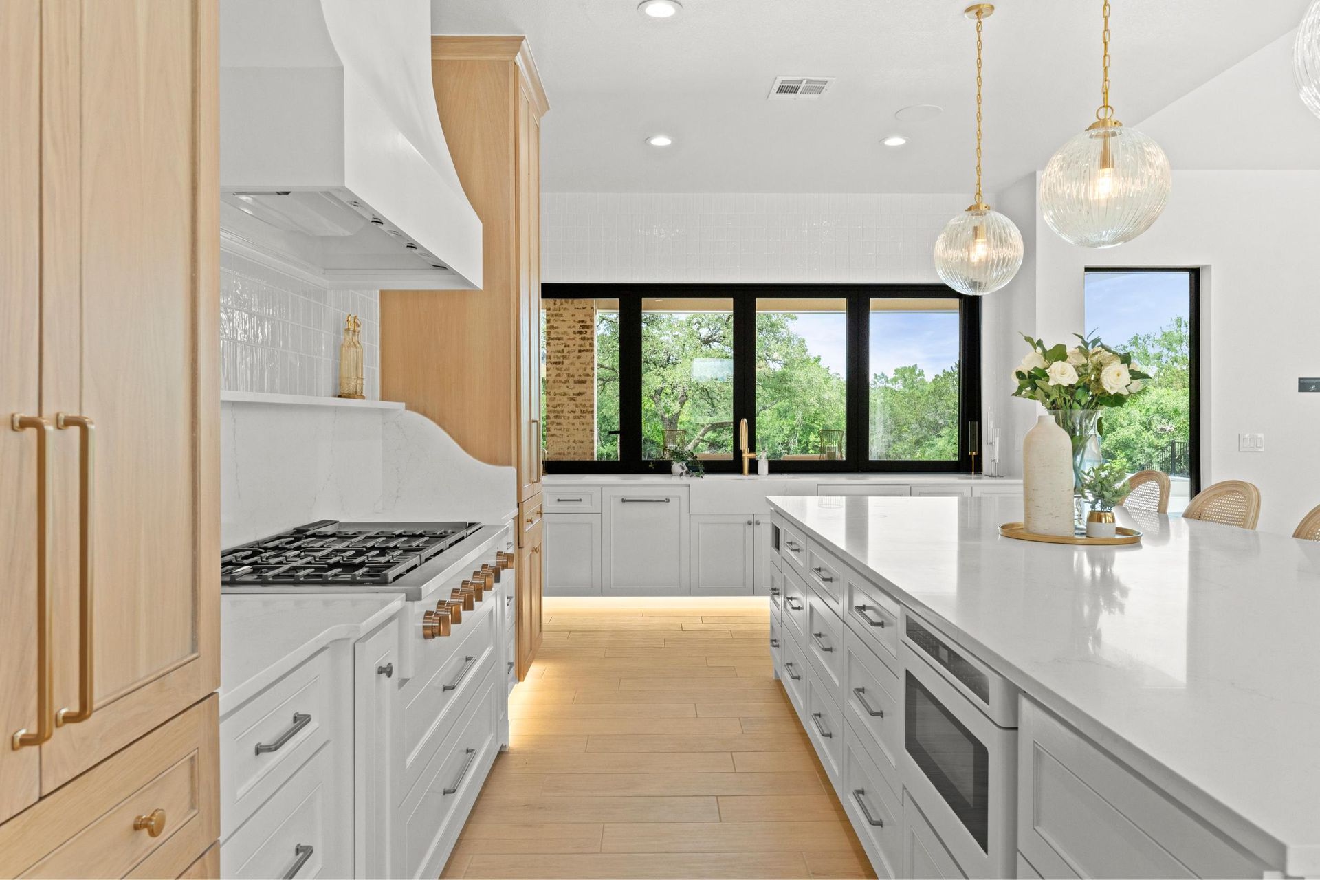 Bright modern kitchen with white cabinets, wood floors, and large black-framed windows.
