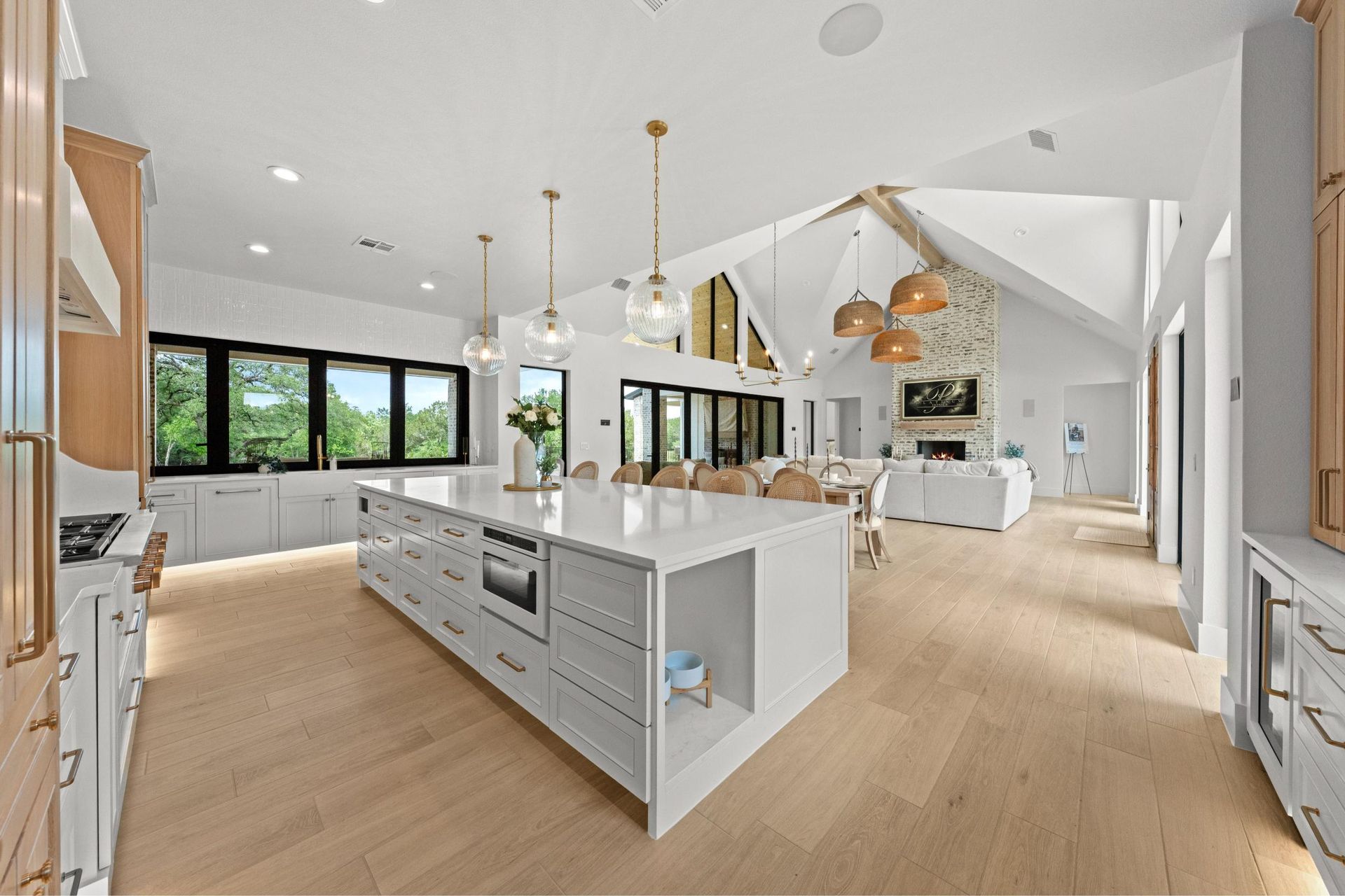 Bright open-concept kitchen and living area with white cabinets, island, wood floors, and large windows
