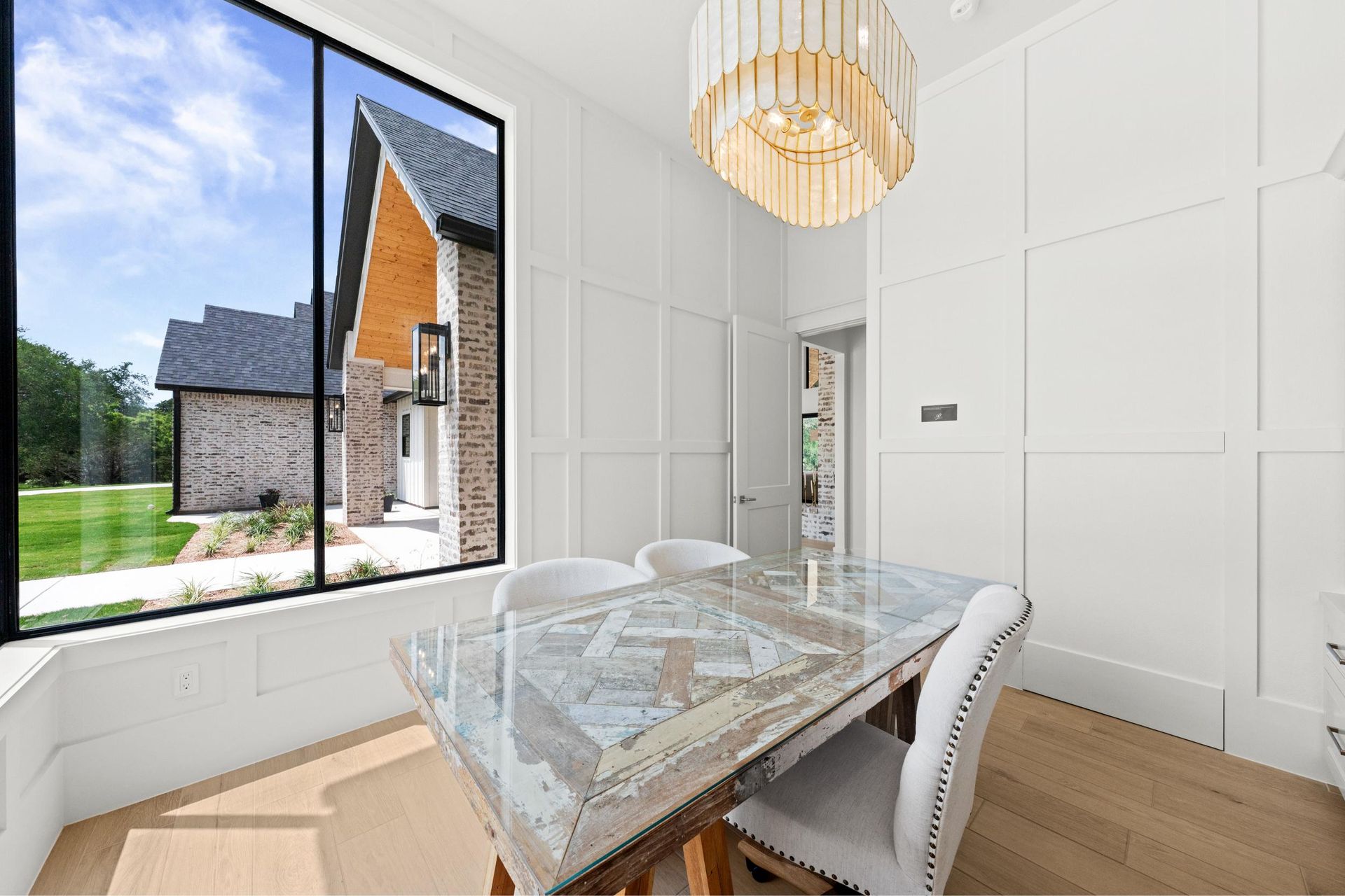 Bright dining room with marble table, white chairs, large window, and a modern chandelier