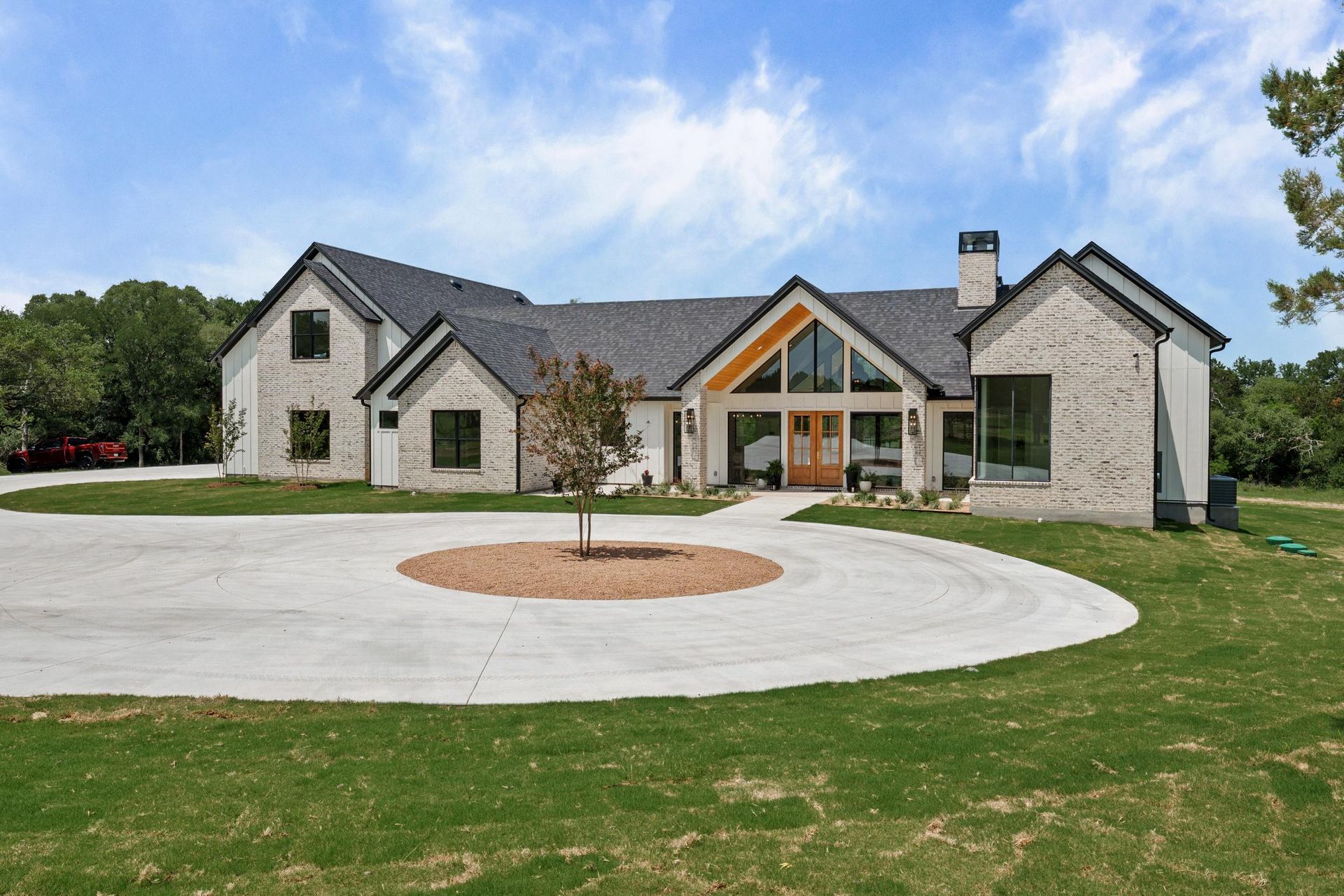 Large modern stone house with a circular driveway and green lawn under a blue sky