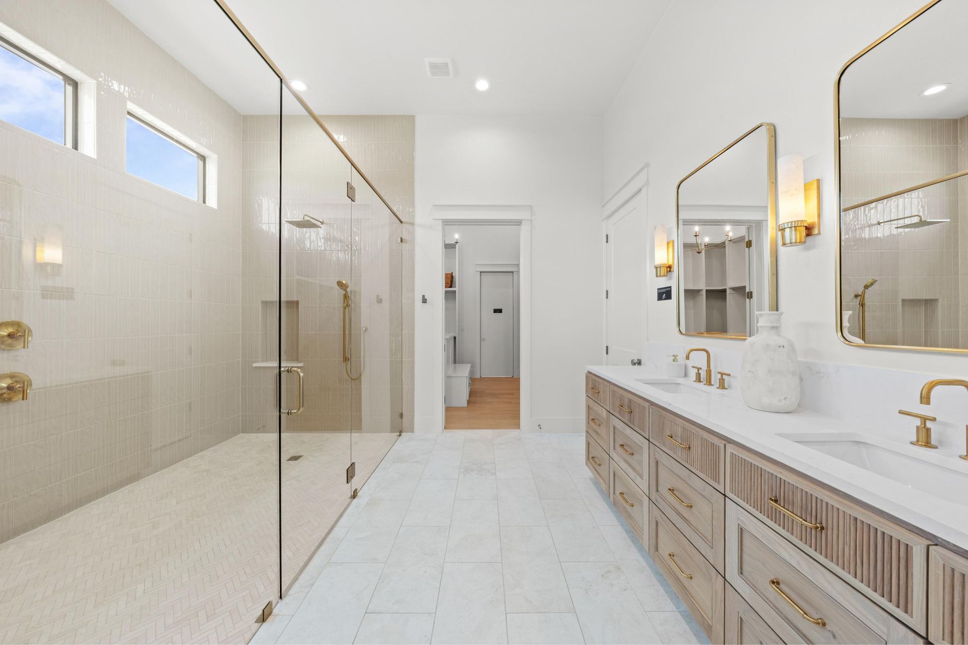 Bright white bathroom with glass shower, double vanity, and large mirror
