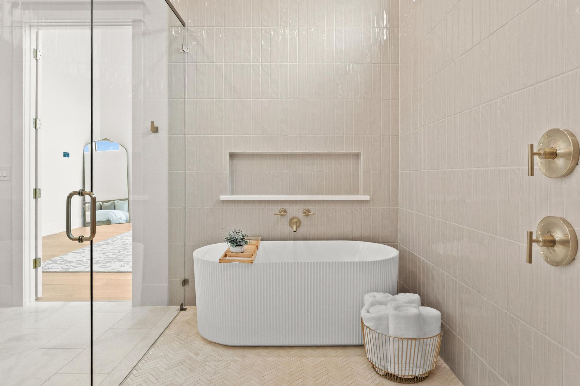 Minimal beige bathroom with freestanding tub, glass shower, and gold fixtures
