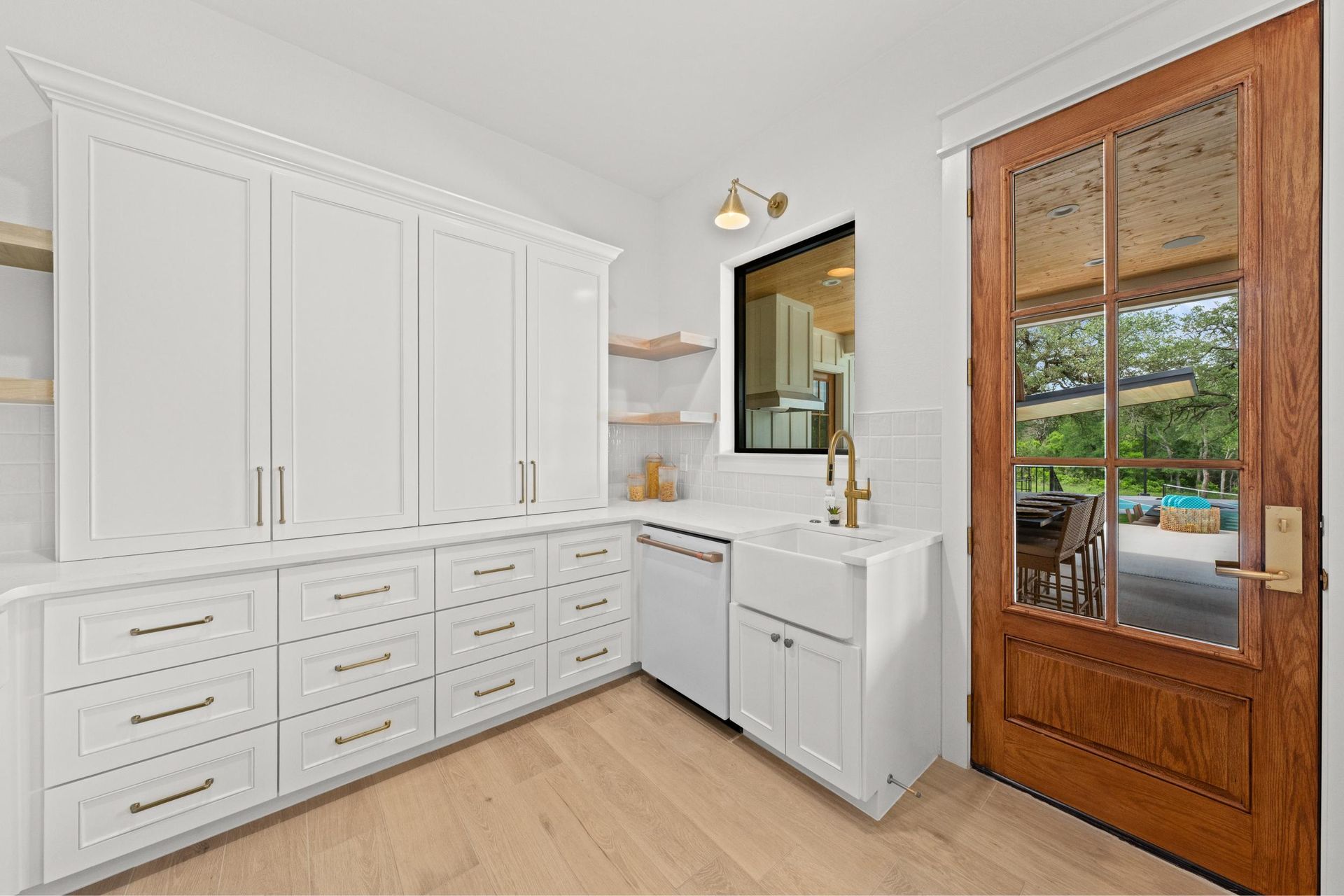 Bright laundry room with white cabinets, sink, mirror, and a wooden door with glass panels.