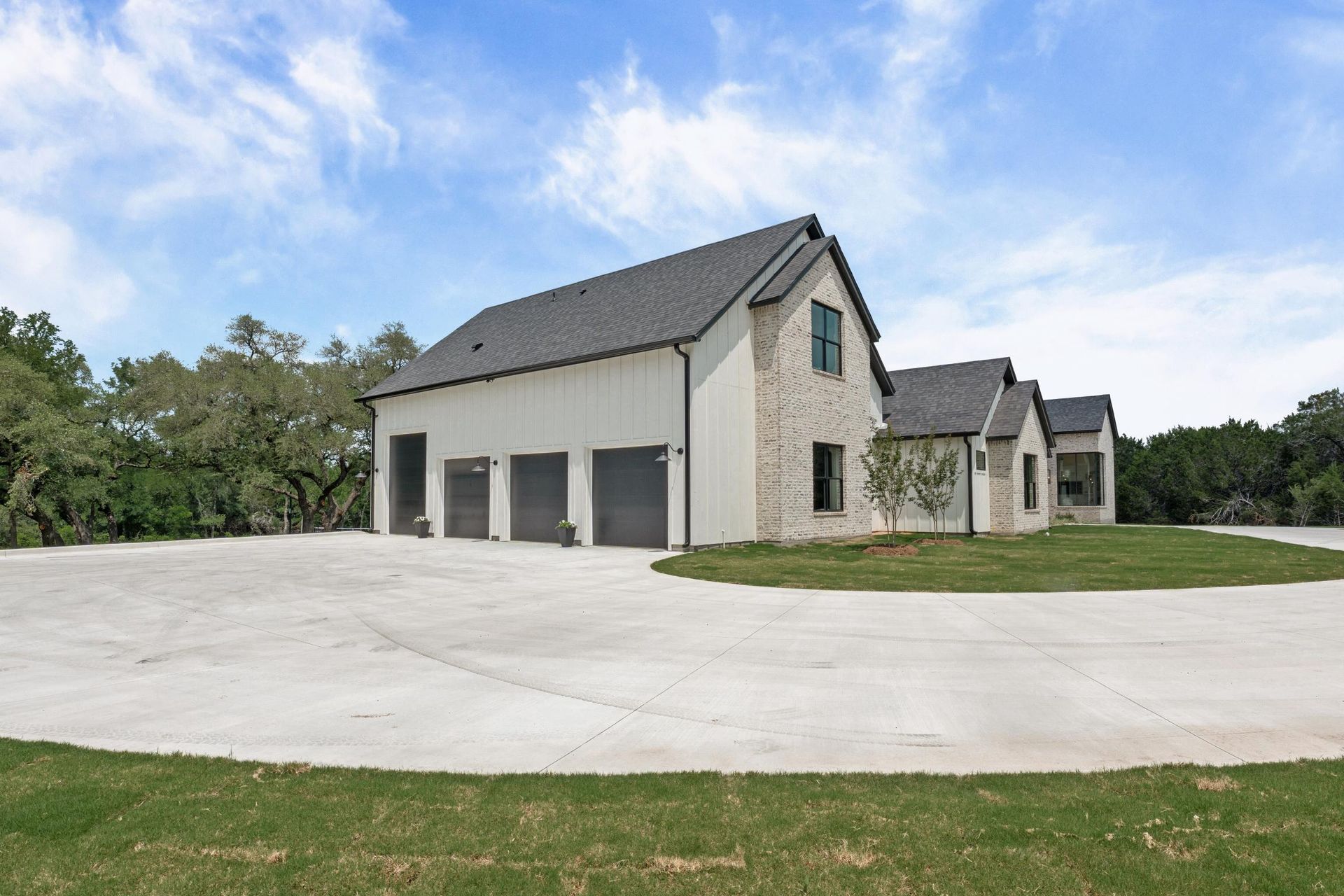 Large modern house with stone facade, gray roof, and wide concrete driveway under a blue sky.