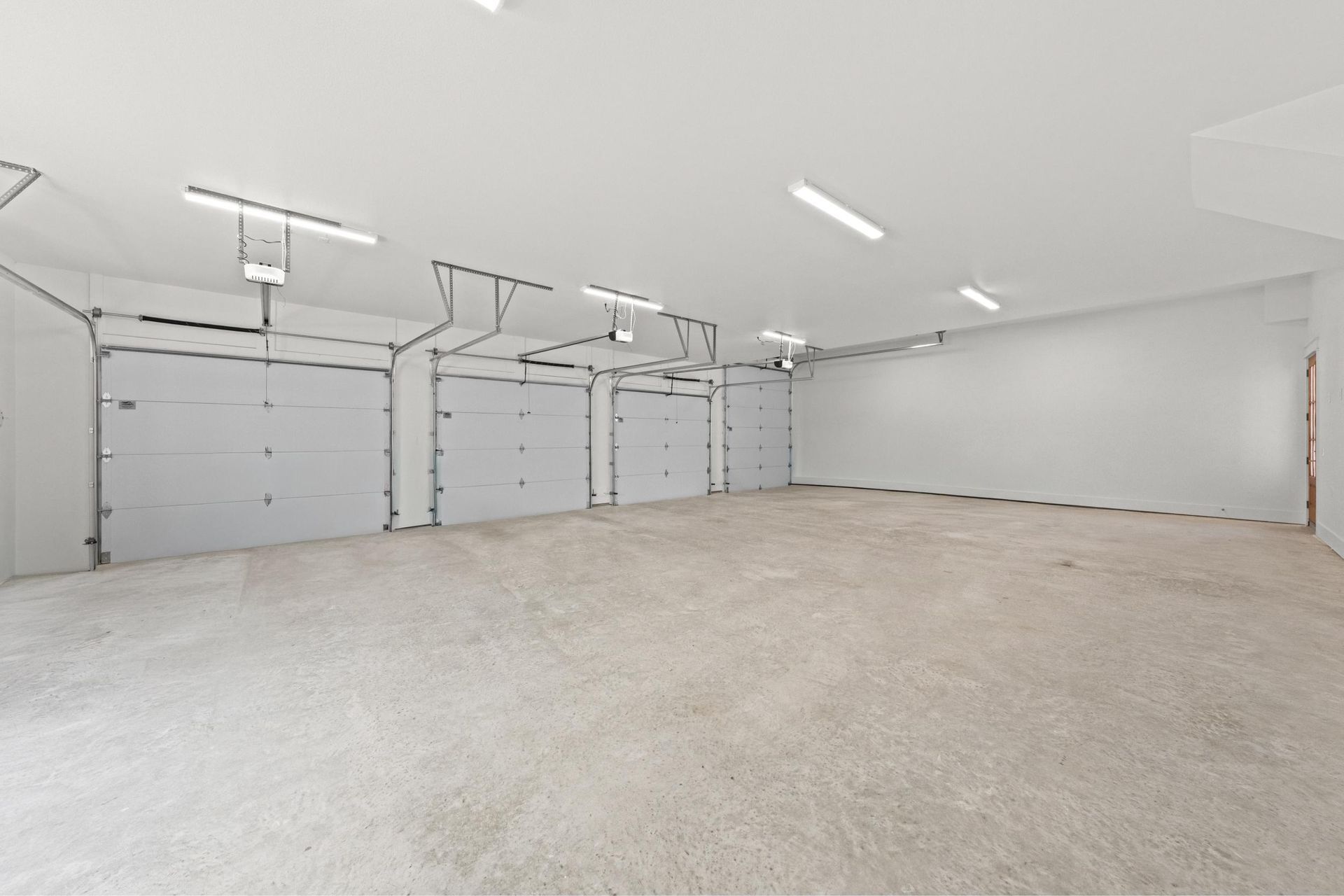 Spacious empty three-car garage with white walls, epoxy floor, and overhead lights