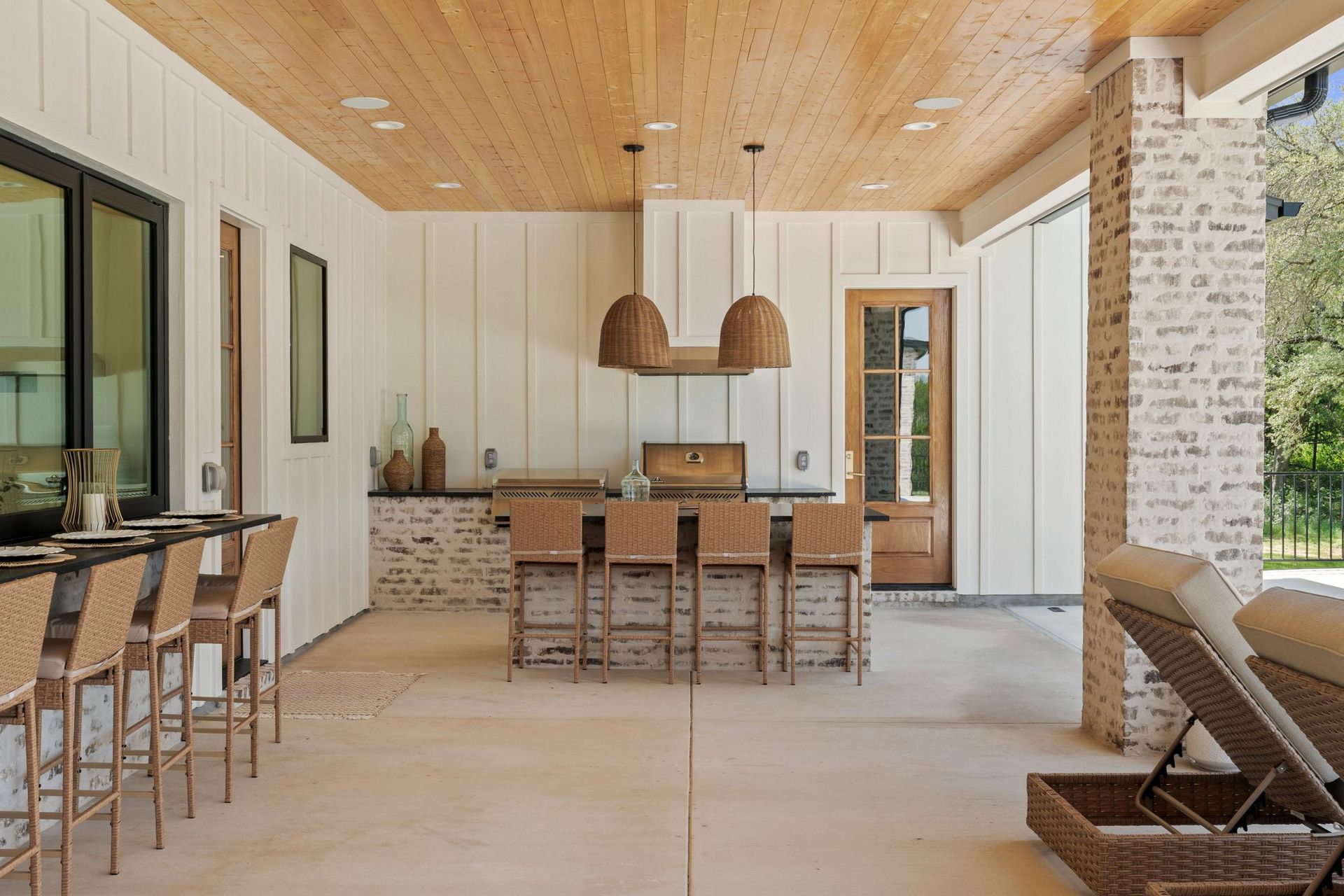 Modern covered patio with wood ceiling, stone fireplace, outdoor dining table, and lounge chairs.