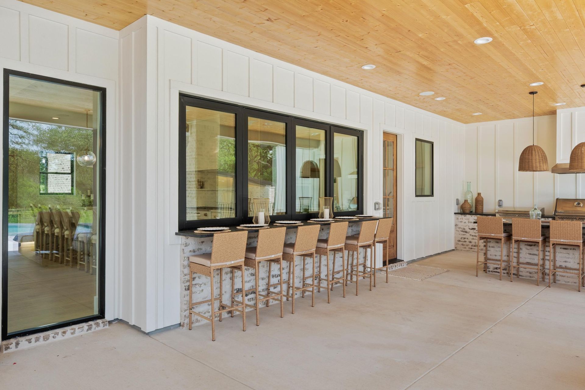 Modern patio with white walls, wood ceiling, bar seating, and black-framed windows.