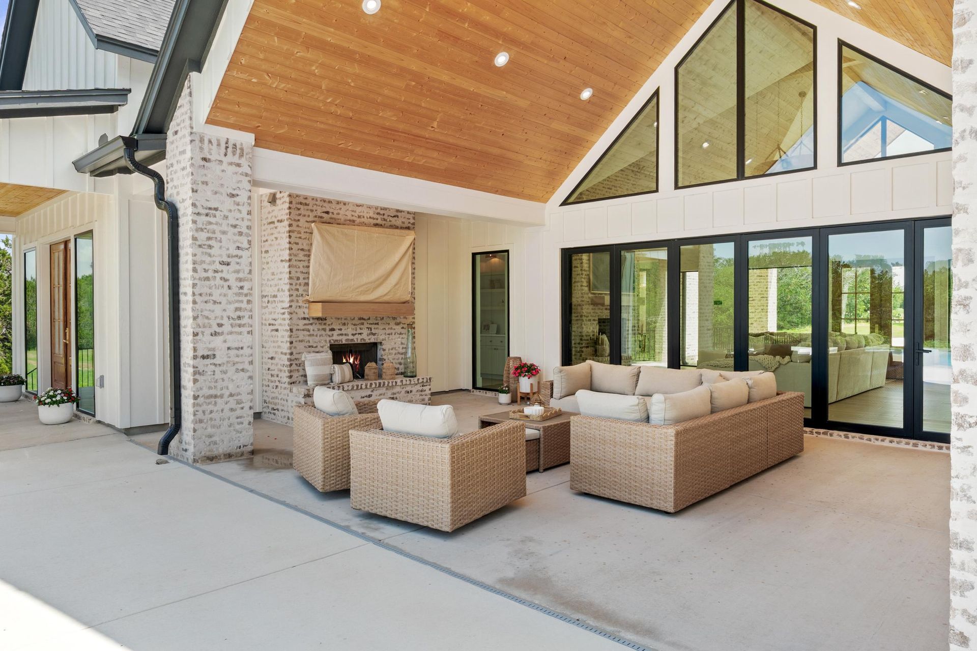 Covered patio with wicker seating, wood ceiling, and large glass doors overlooking a modern home courtyard