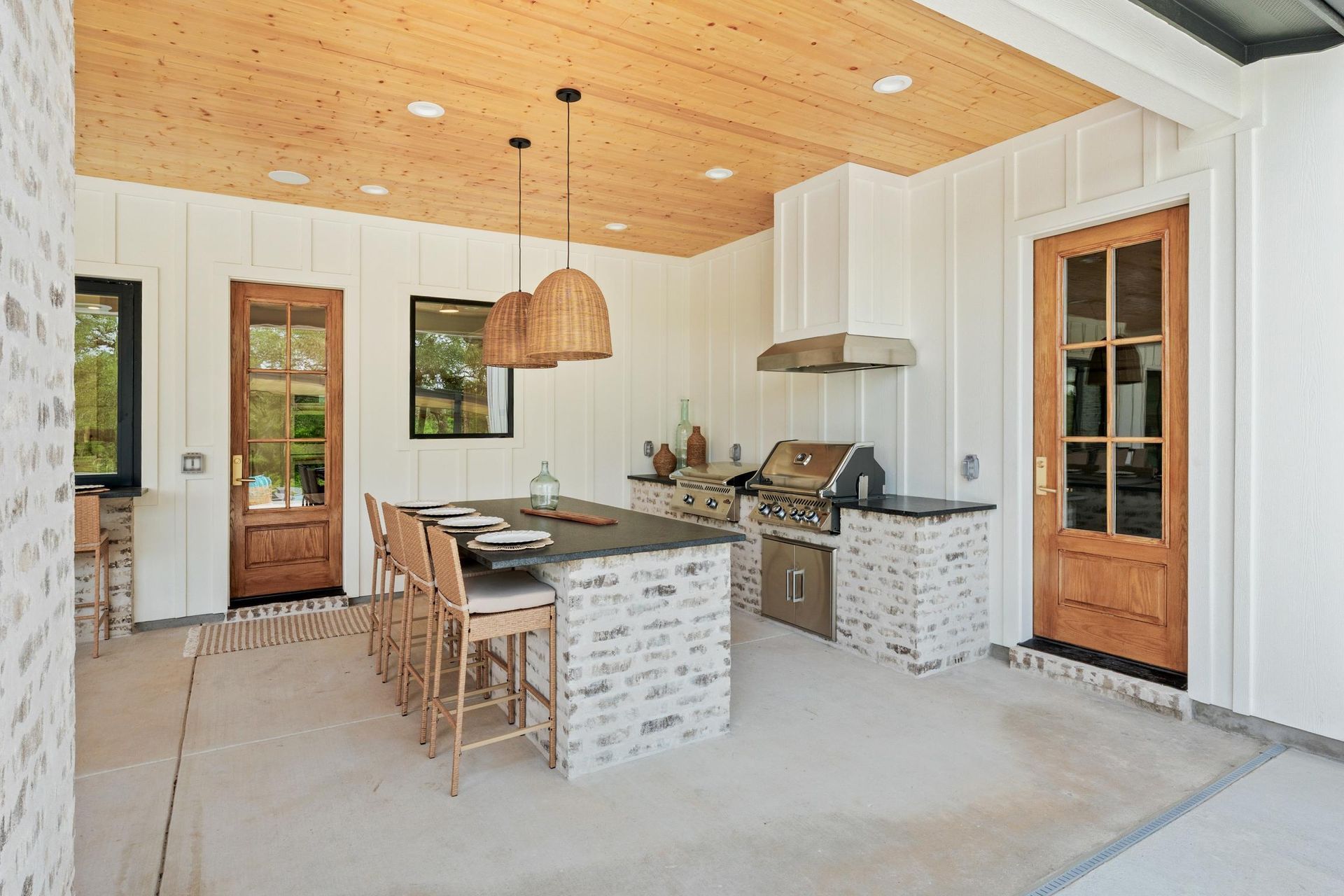 Modern kitchen with island, wood ceiling, white walls, and glass doors leading outside.