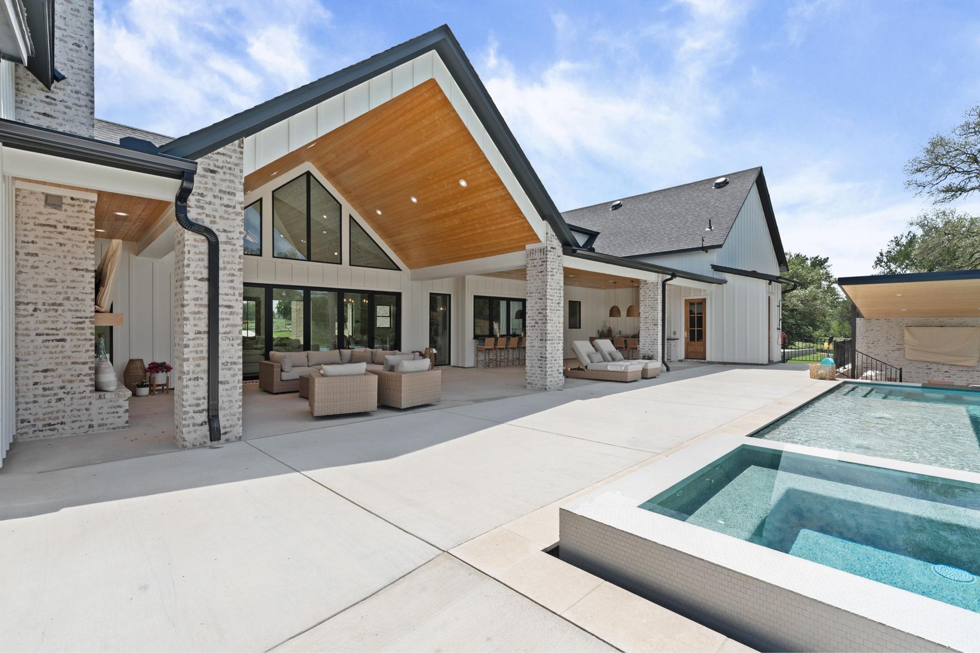 Modern backyard patio with pool, covered seating area, and white brick house exterior