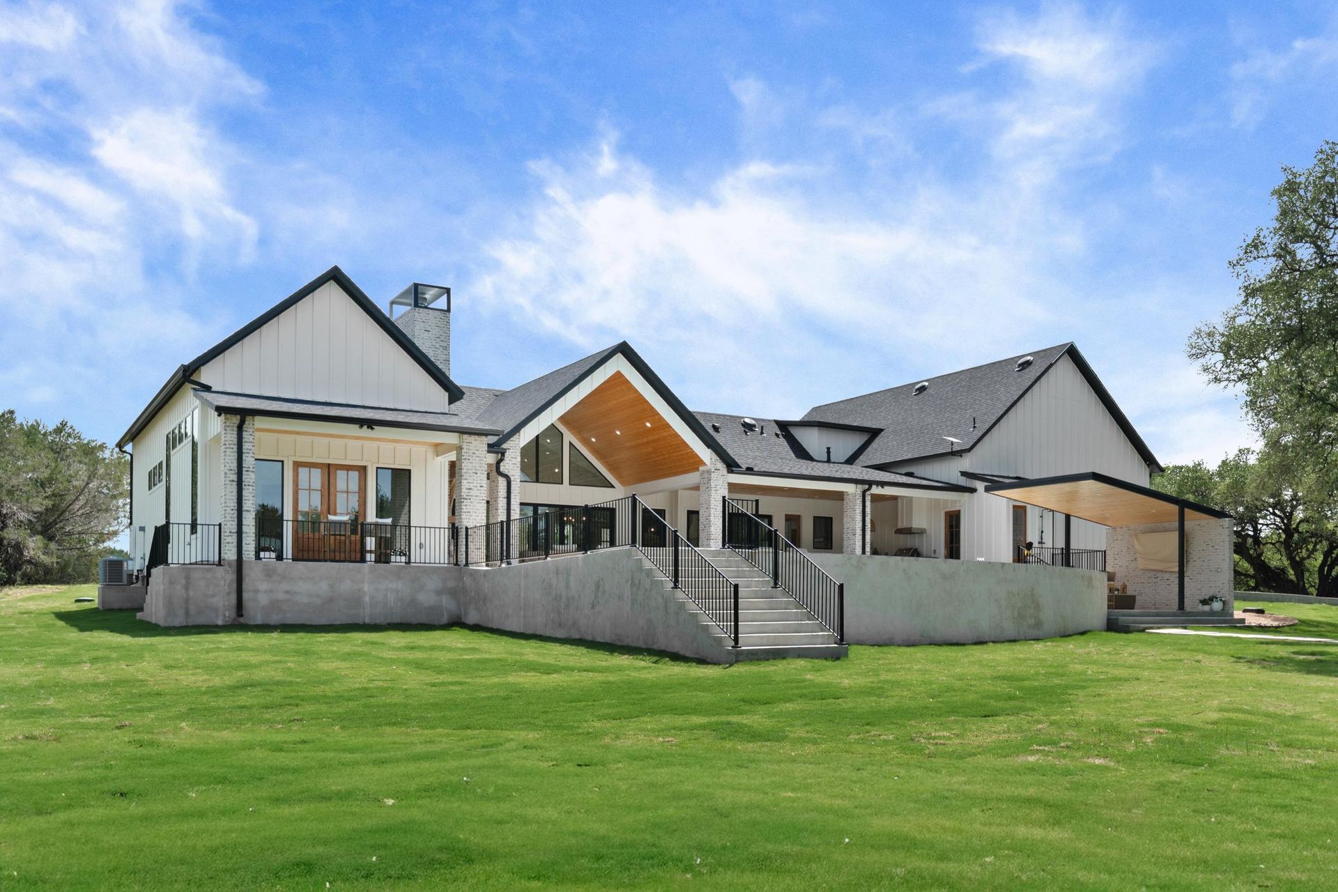 Large modern house with gray roof, front steps, and wide green lawn under a blue sky