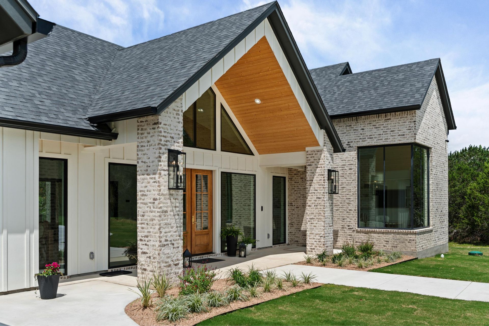 Modern stone-and-white house exterior with peaked roof, wood front door, and manicured lawn