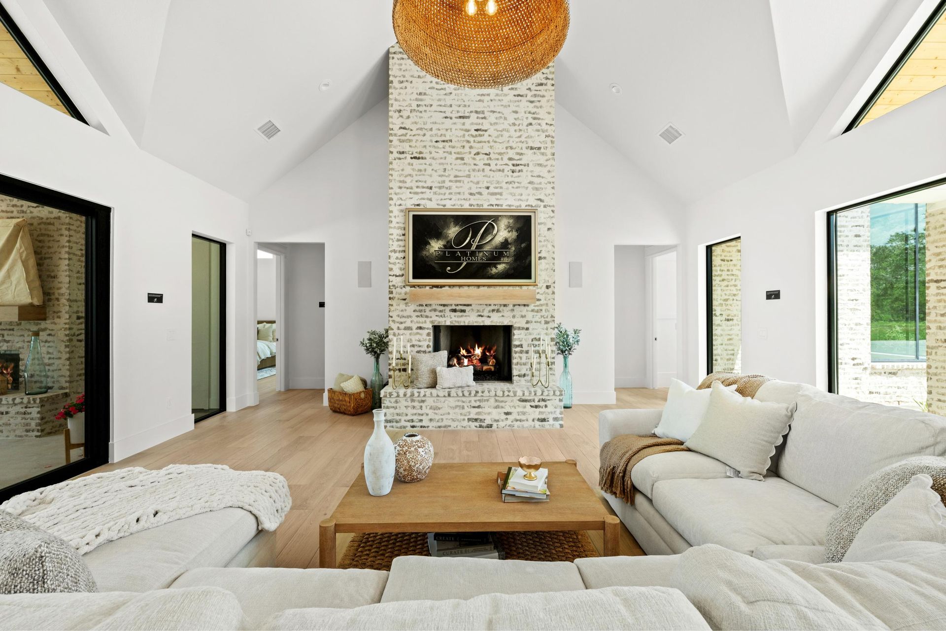 Bright modern living room with vaulted ceiling, stone fireplace, beige sofas, and large windows