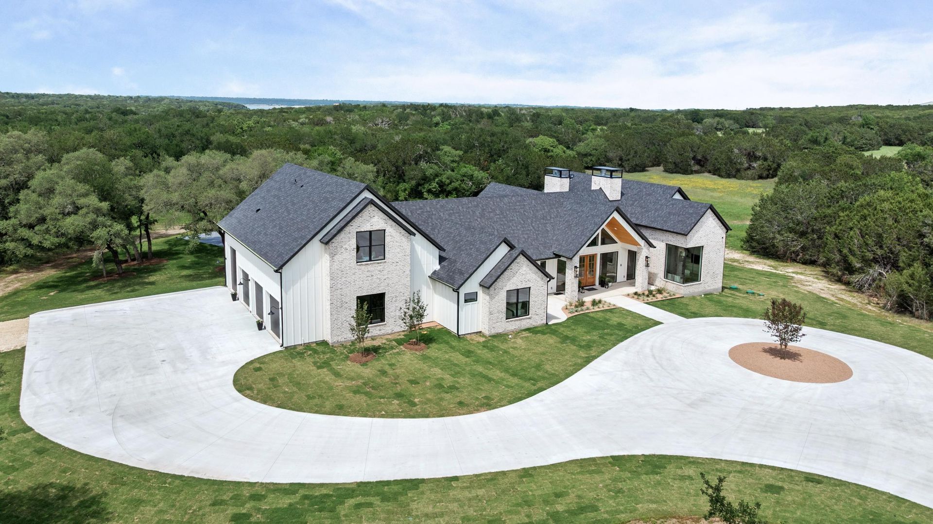 Modern gray house with white stone facade, large driveway, and wooded landscape backdrop