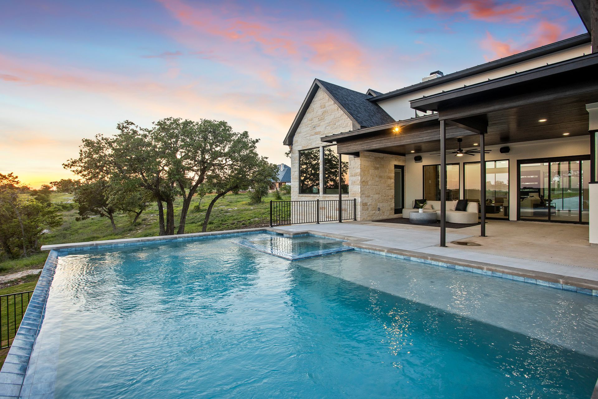 Modern house with an infinity pool at sunset overlooking trees and hills