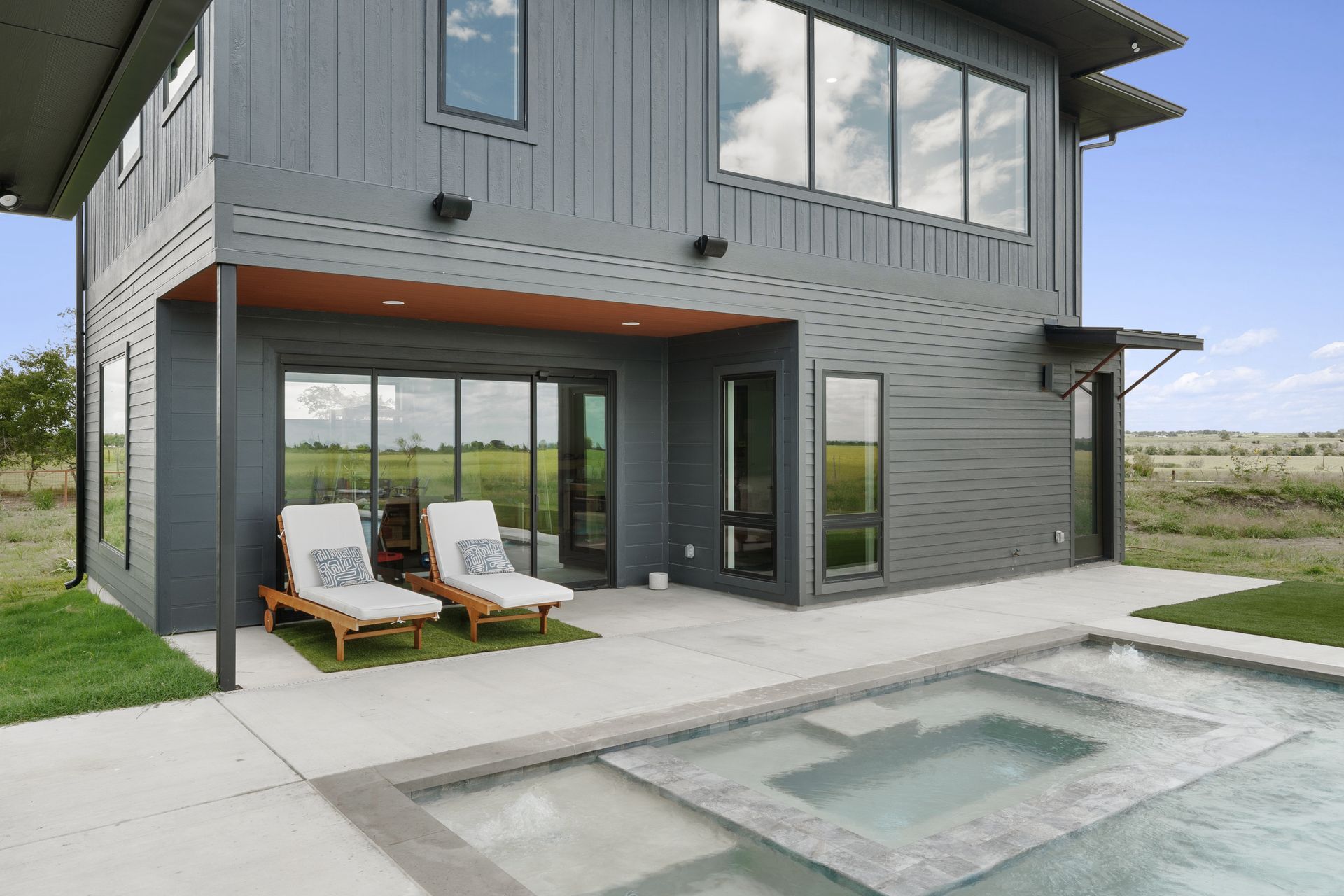 Modern gray two-story house with patio chairs and a swimming pool in the foreground