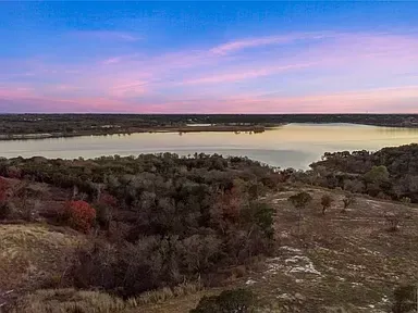 Sunset over a lake with rocky shoreline and dense shrubs in the foreground