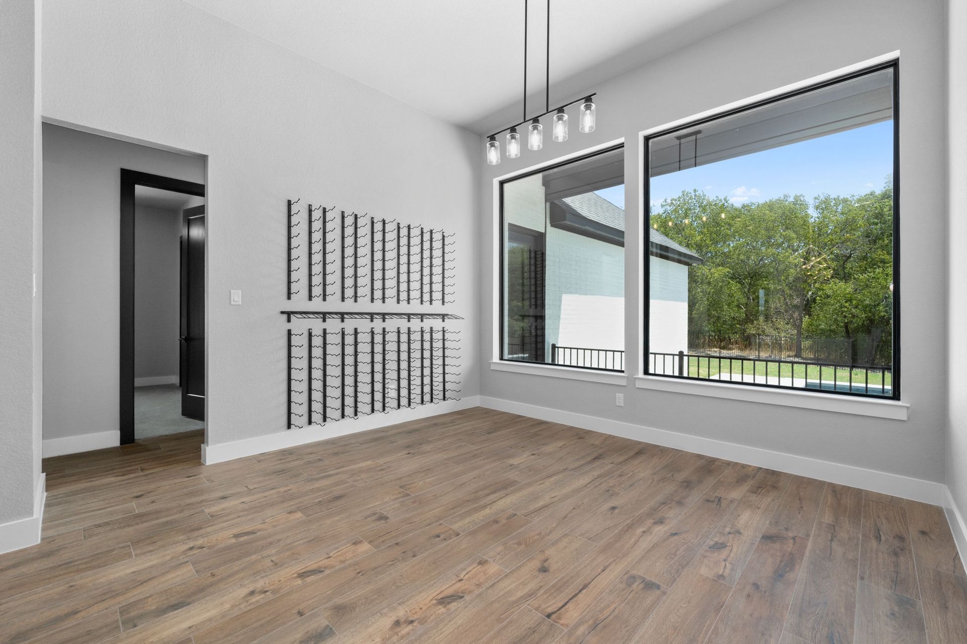 Bright empty living room with wood floors, large windows, and a modern light fixture