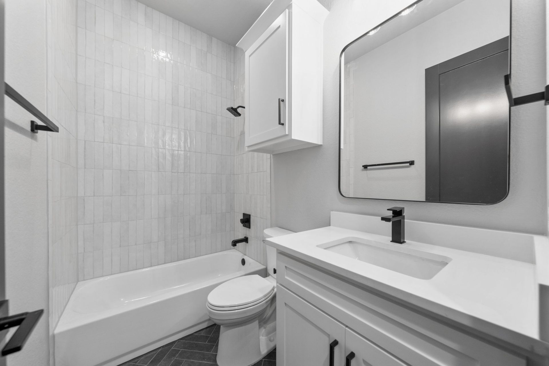 Small modern bathroom with tub, toilet, vanity sink, and mirror in white and gray tones