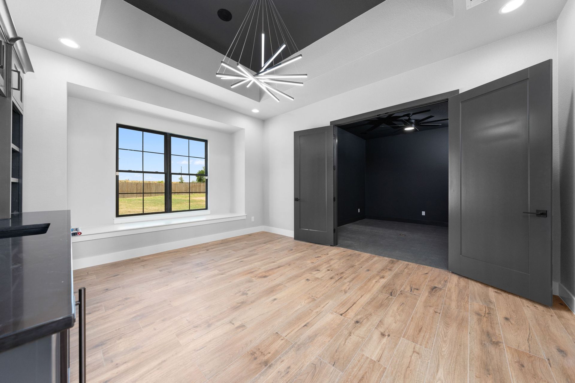 Modern empty bedroom with gray walls, light wood floors, and a large window.