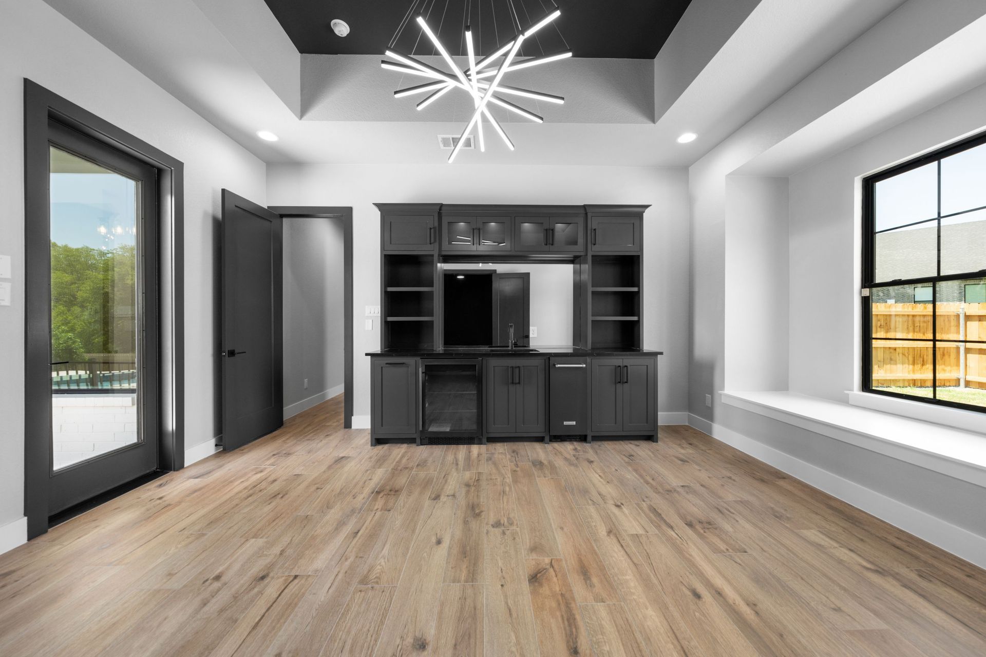 Modern empty living room with wood floors, black built-in shelving, and large windows on both sides