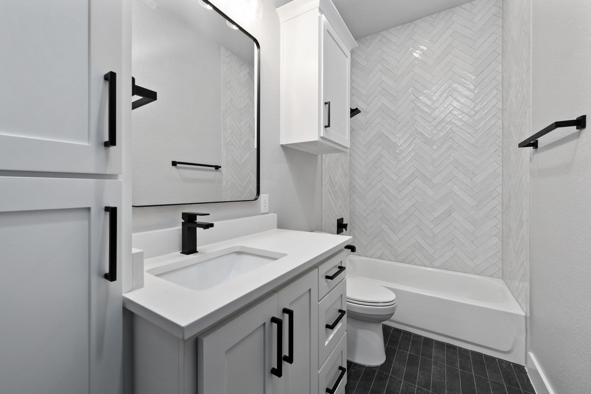 Modern white bathroom with vanity, mirror cabinet, tub, toilet, and black floor tiles